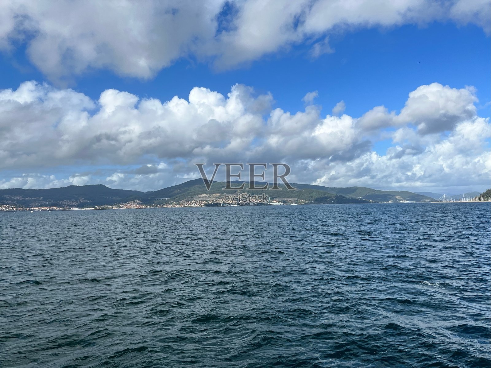 海岸风光：宁静的海洋、遥远的城市和多云的山脉。照片摄影图片