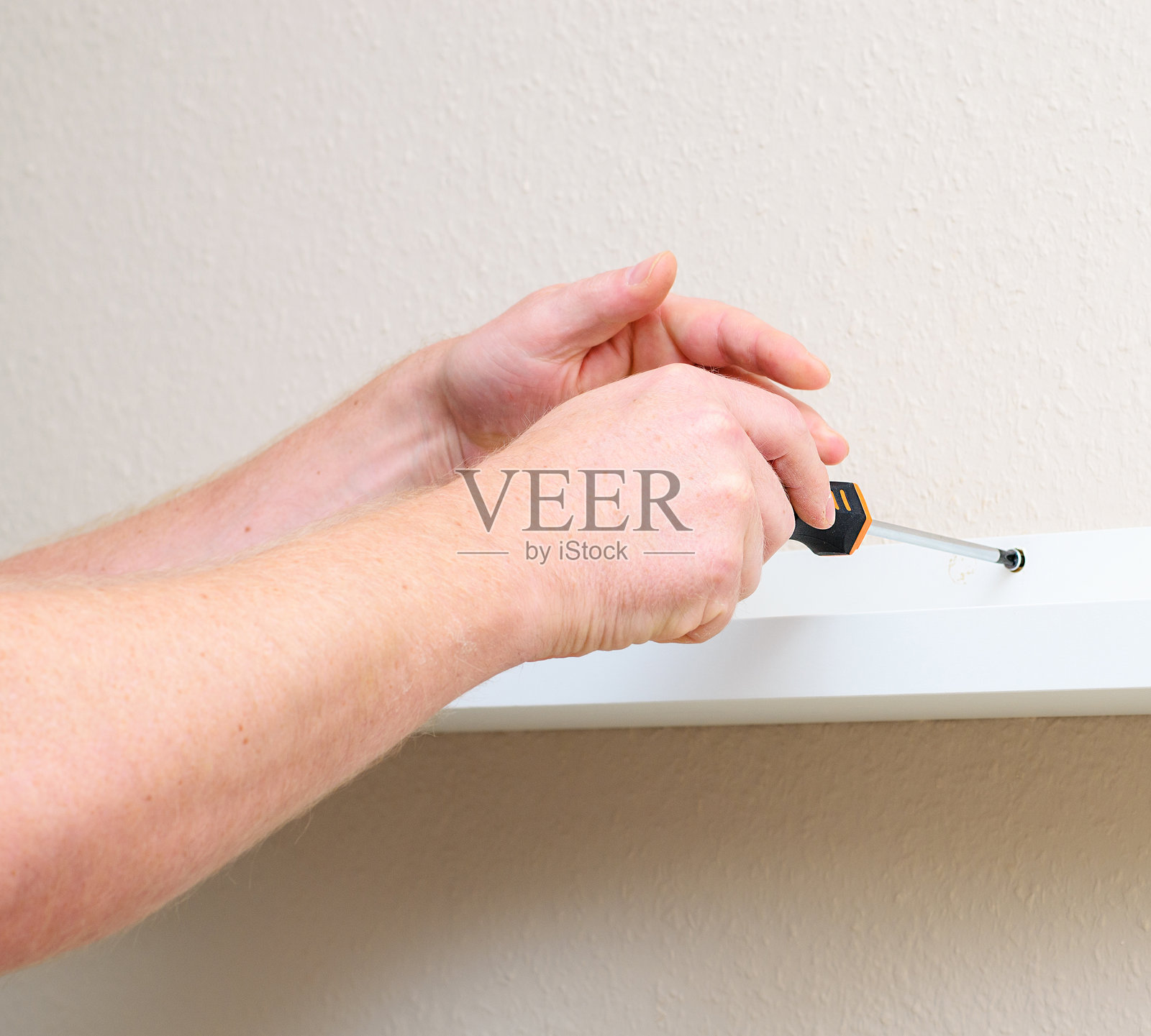 男人用螺丝刀将白色架子固定在墙上，特写手部和工作细节。照片摄影图片