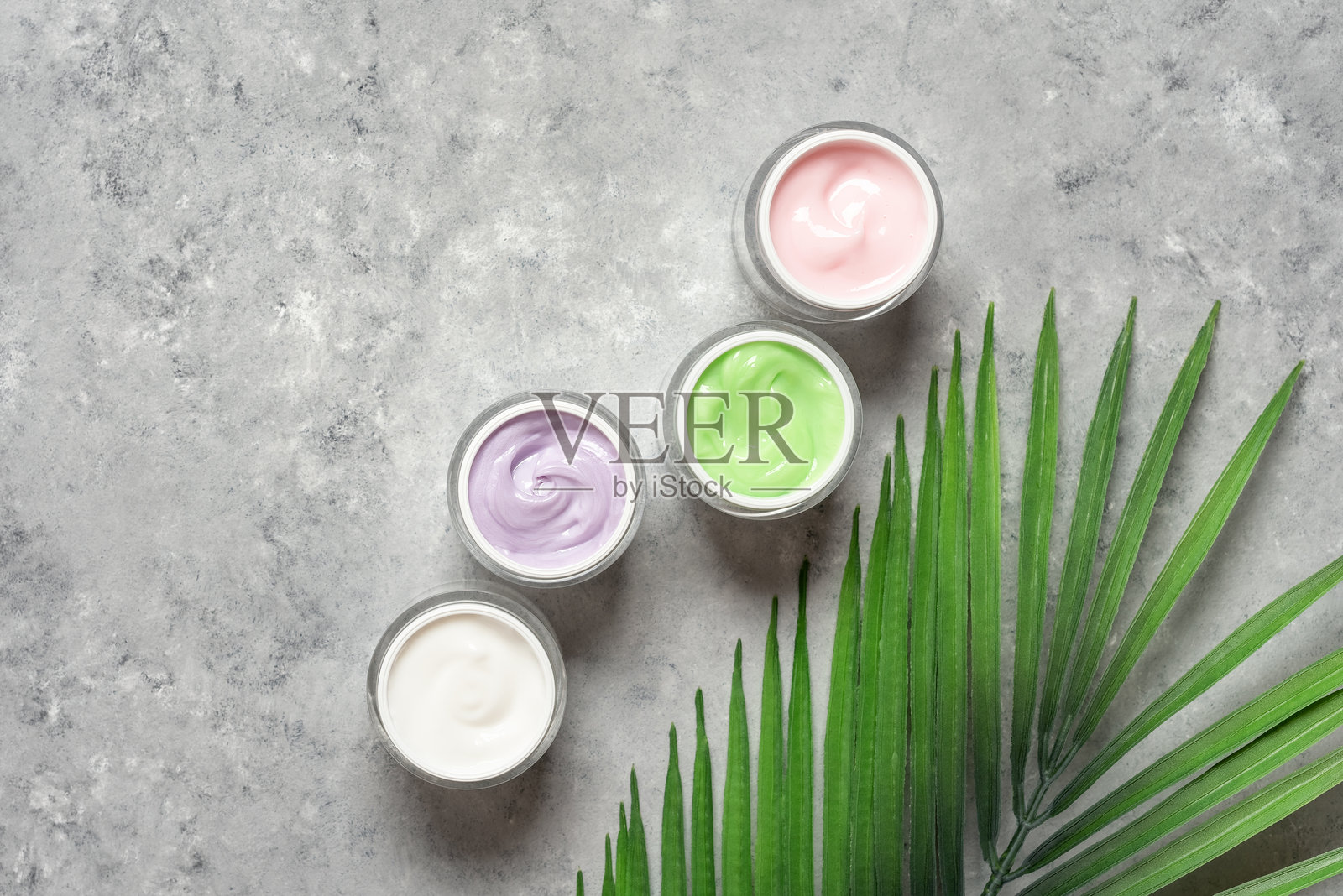 不同的护肤霜在灰色磨砂背景上，搭配棕榈叶，俯视图，平铺，留白。抗衰老和保湿护肤霜。照片摄影图片