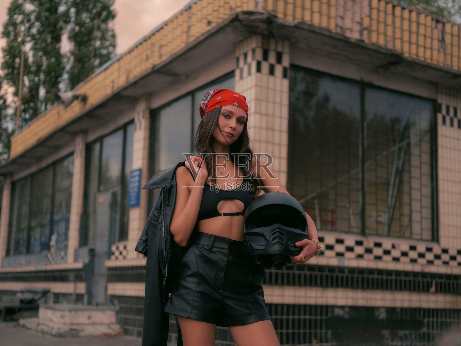 自信的女性，戴着红色头巾和短款上衣，手持摩托车头盔。照片摄影图片