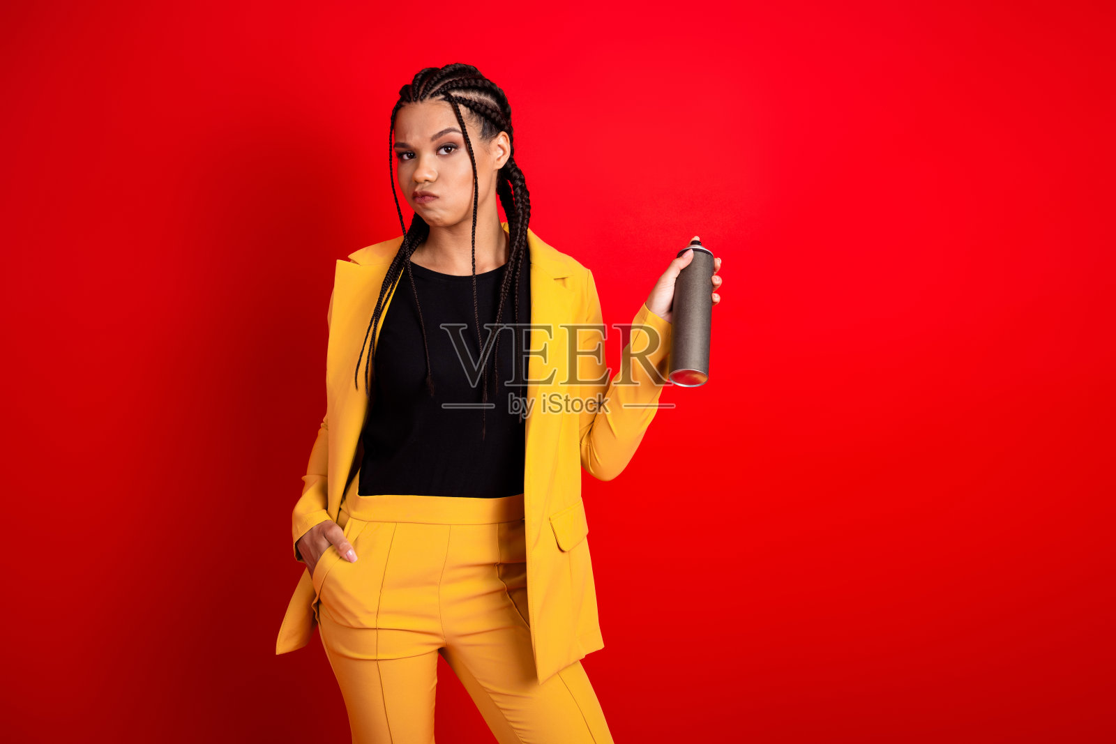 身穿鲜艳黄色西装的时尚年轻女性手持喷雾罐，背景为大胆的红色，散发出自信的气息。照片摄影图片