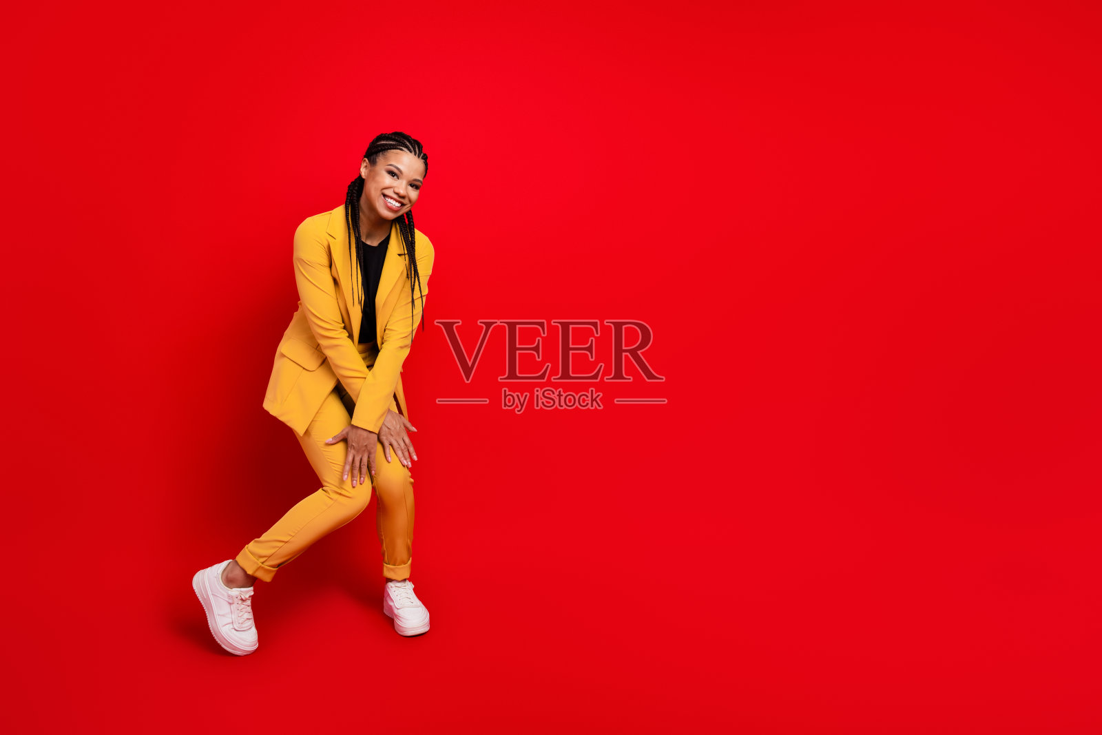 身穿黄色西装的时尚女性在鲜艳的红色背景前充满活力地摆姿势，展现出自信的风格和现代商务魅力。照片摄影图片