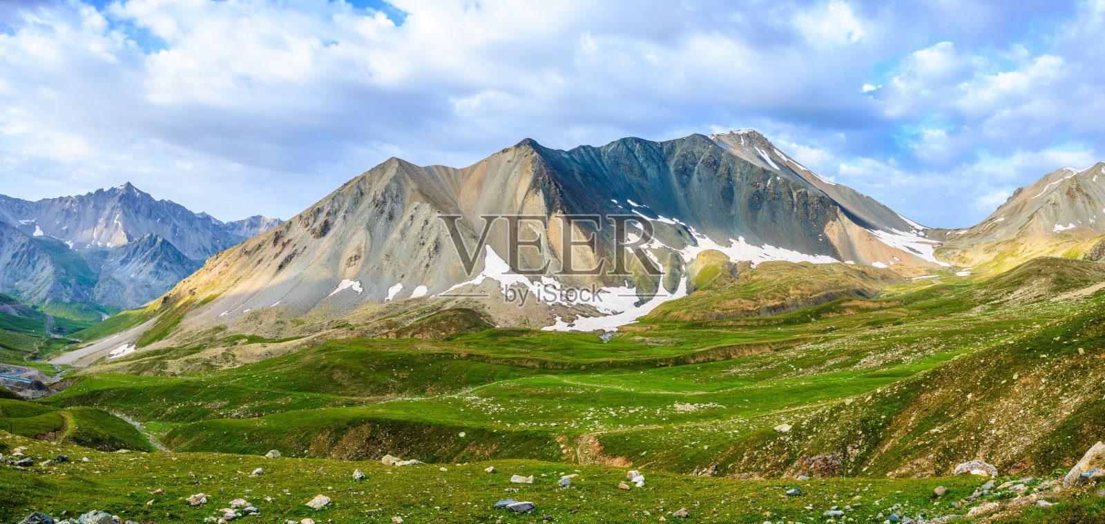 雄伟的雪山与生机勃勃的绿色起伏山丘在美丽的多云天空下交相辉映照片摄影图片