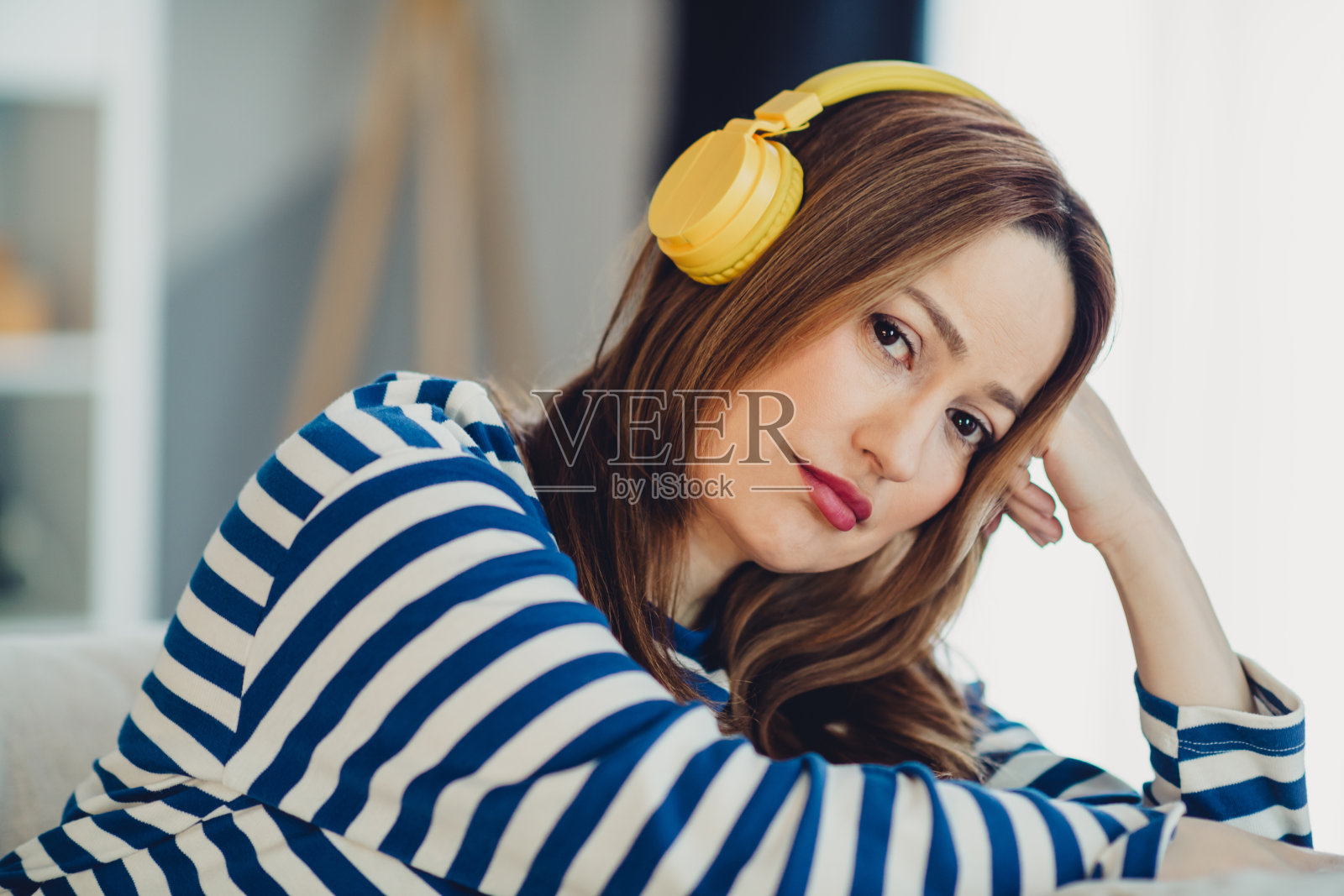 一位成熟的女性在室内放松，戴着黄色耳机，穿着条纹衬衫，享受宁静的家庭时光照片摄影图片