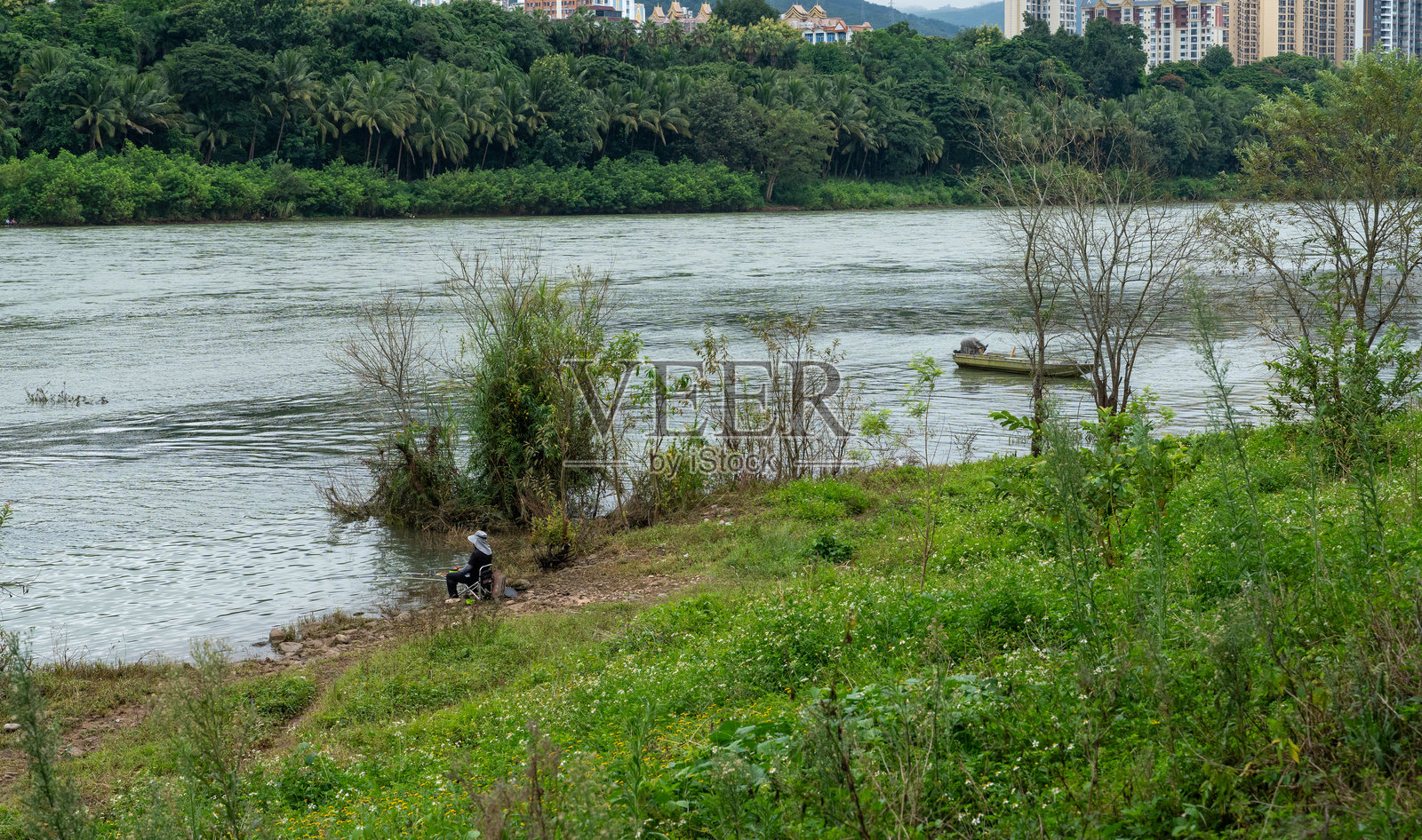 人们在湄公河边钓鱼和放松，背景是现代城市天际线。照片摄影图片