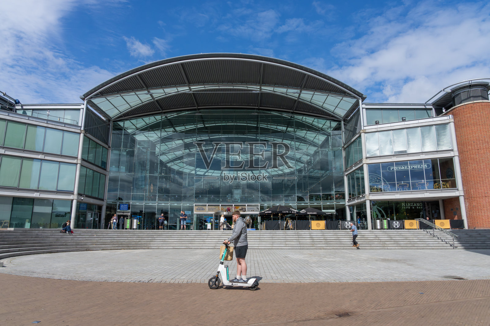 现代公共建筑前的台阶,诺里奇市中心,一名骑电动滑板车的男子在前景经过。照片摄影图片