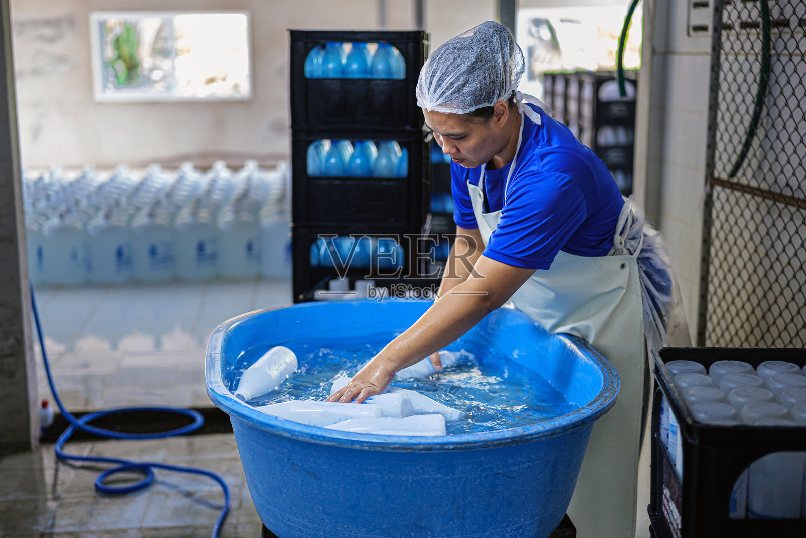 亚洲胖女性工人在户外清洗塑料水瓶，并在进入自动清洗系统之前检查塑料瓶的质量。照片摄影图片