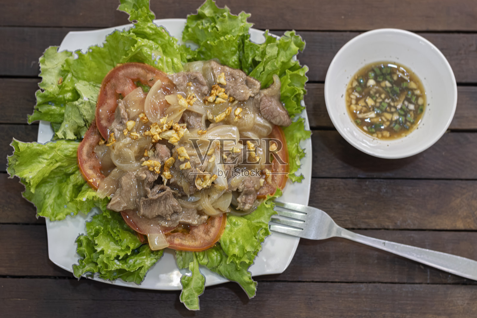 传统柬式Lok Lak牛肉配蒜、洋葱、生菜、西红柿和柬埔寨卡波特胡椒酱。照片摄影图片