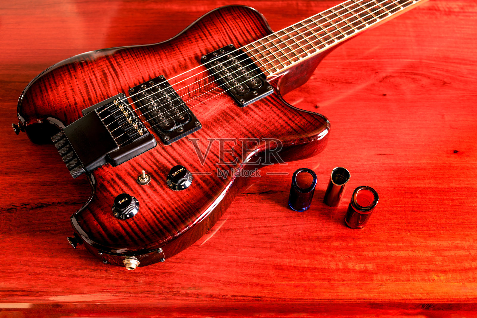 一把无头电吉他和三根滑棒放在玫瑰木桌子上照片摄影图片