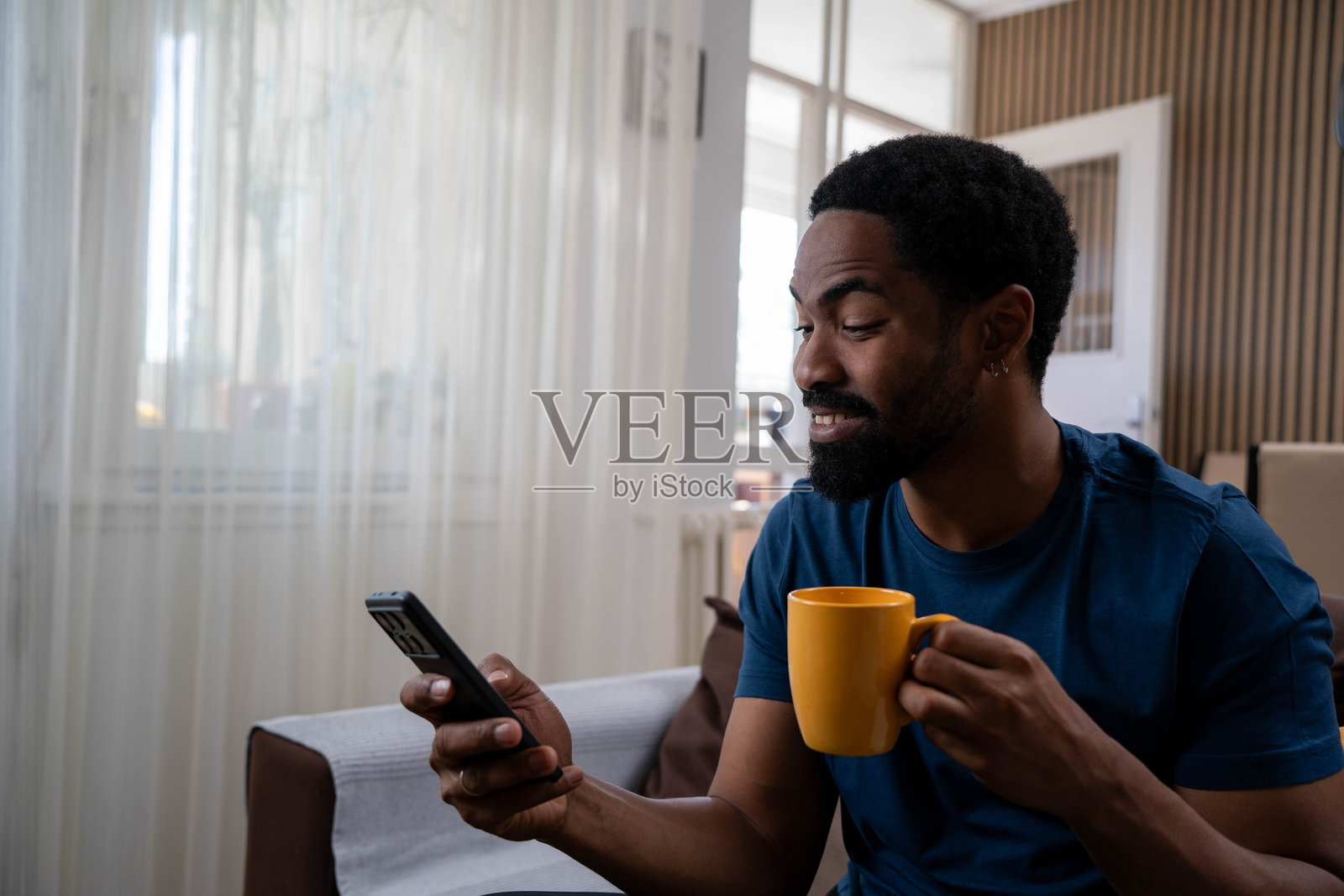 微笑的快乐男人在家里的客厅里阅读来自爱人的信息，喝着咖啡，享受这一刻。照片摄影图片