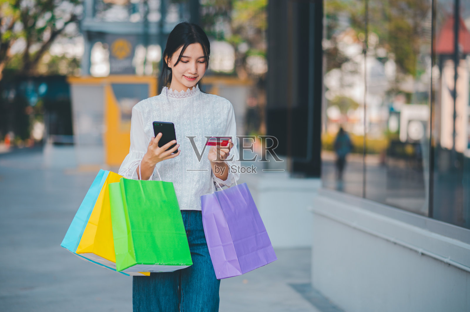 一位女性手里拿着购物袋和手机，正走在街上。照片摄影图片