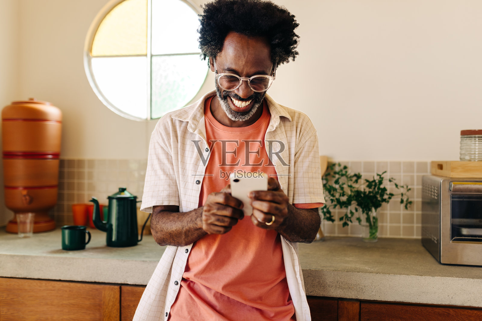 在厨房里，微笑的巴西男子用手机发信息，蓬松的非洲卷发。照片摄影图片