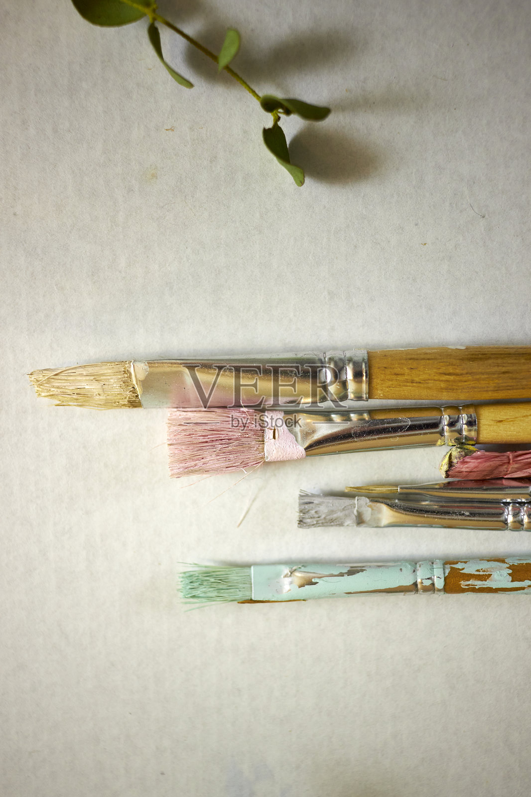 特写镜头展示了排列在白色背景上的五颜六色的旧画笔，笔尖上沾有干涸的颜料。这些是用于绘画、创作、手工项目和设计灵感的艺术工具。照片摄影图片