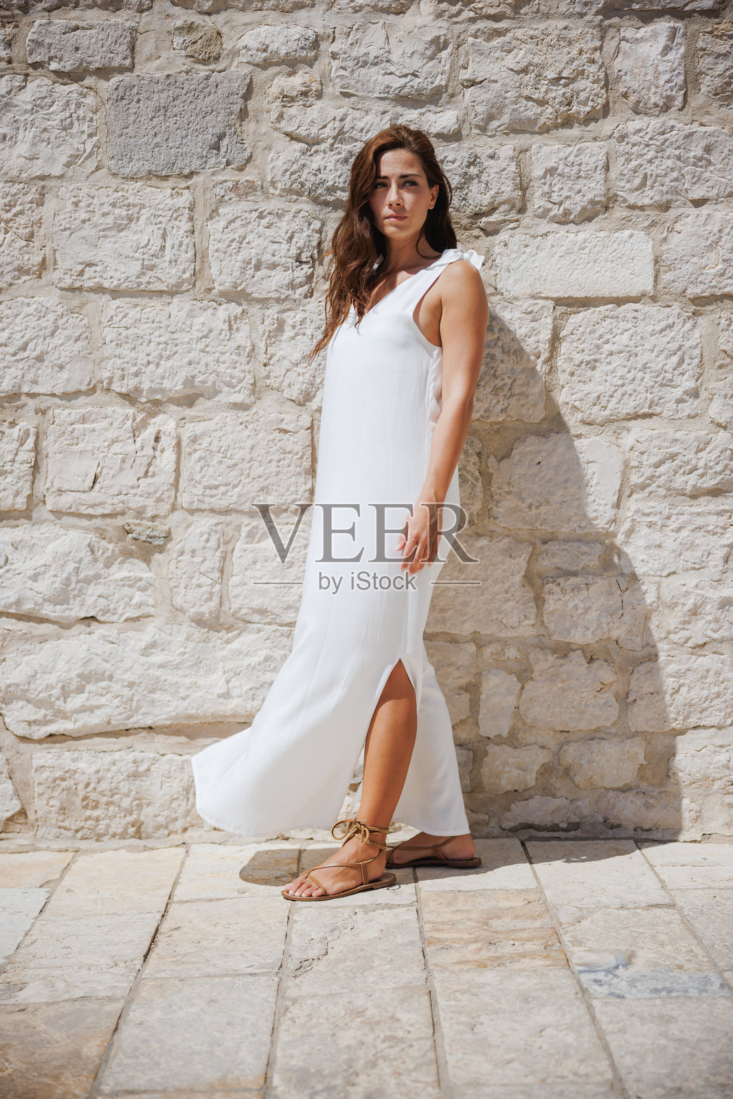 穿着飘逸白色连衣裙的女人站在石砖墙前照片摄影图片