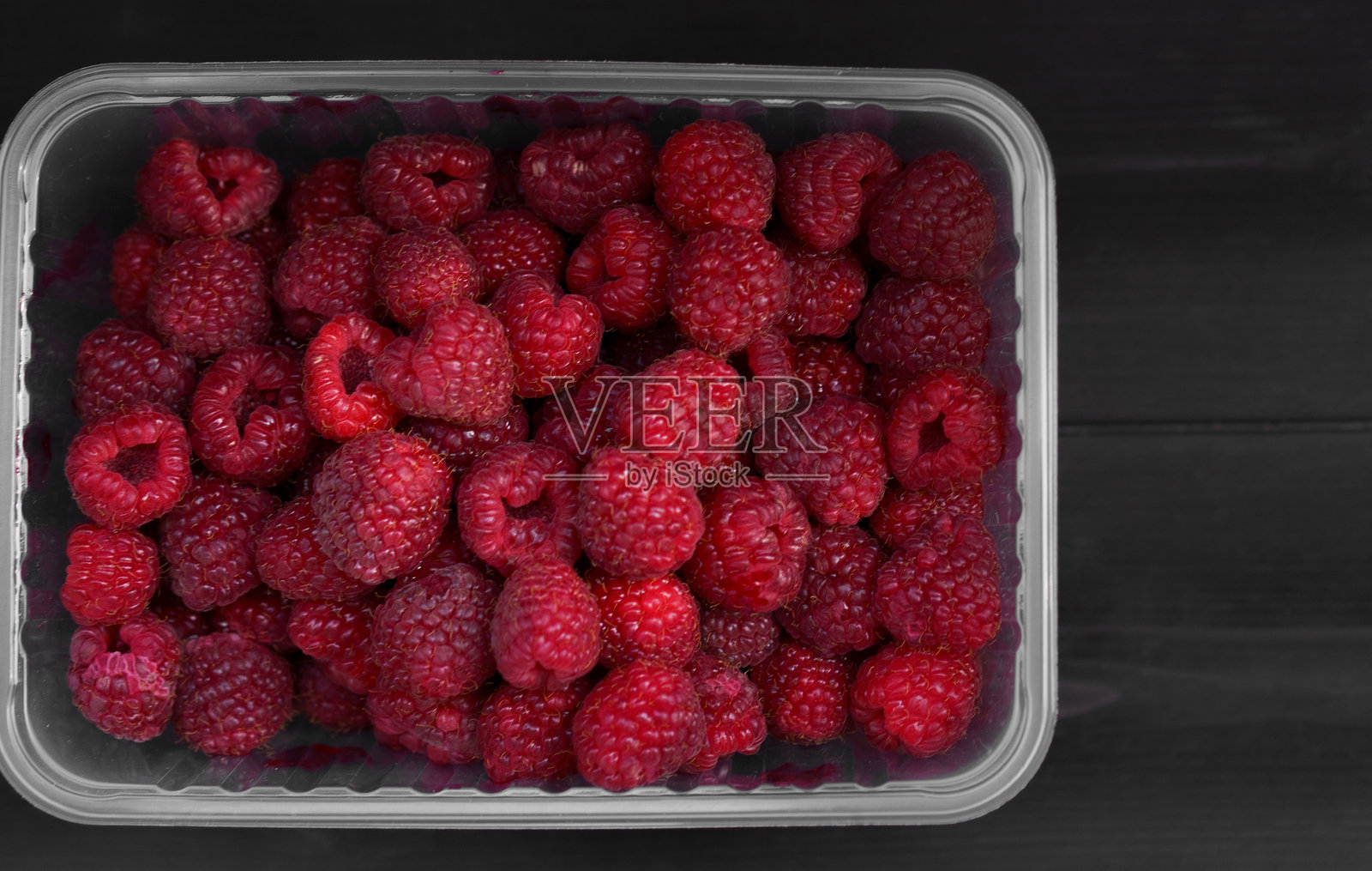 新鲜的覆盆子放在透明容器中，置于深色木质表面上照片摄影图片