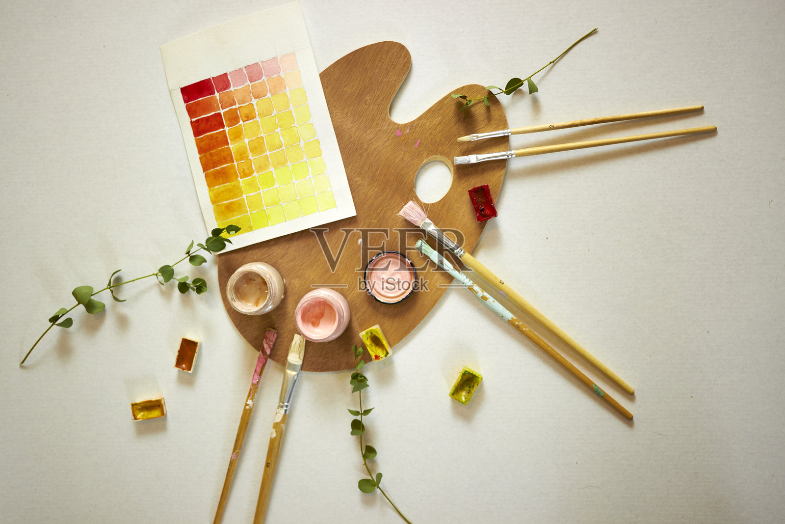艺术家木质调色板的俯视图，上面有水彩颜料、画笔和暖色调的样本纸。适合绘画、艺术项目和设计灵感的创意工作空间平面布局。照片摄影图片