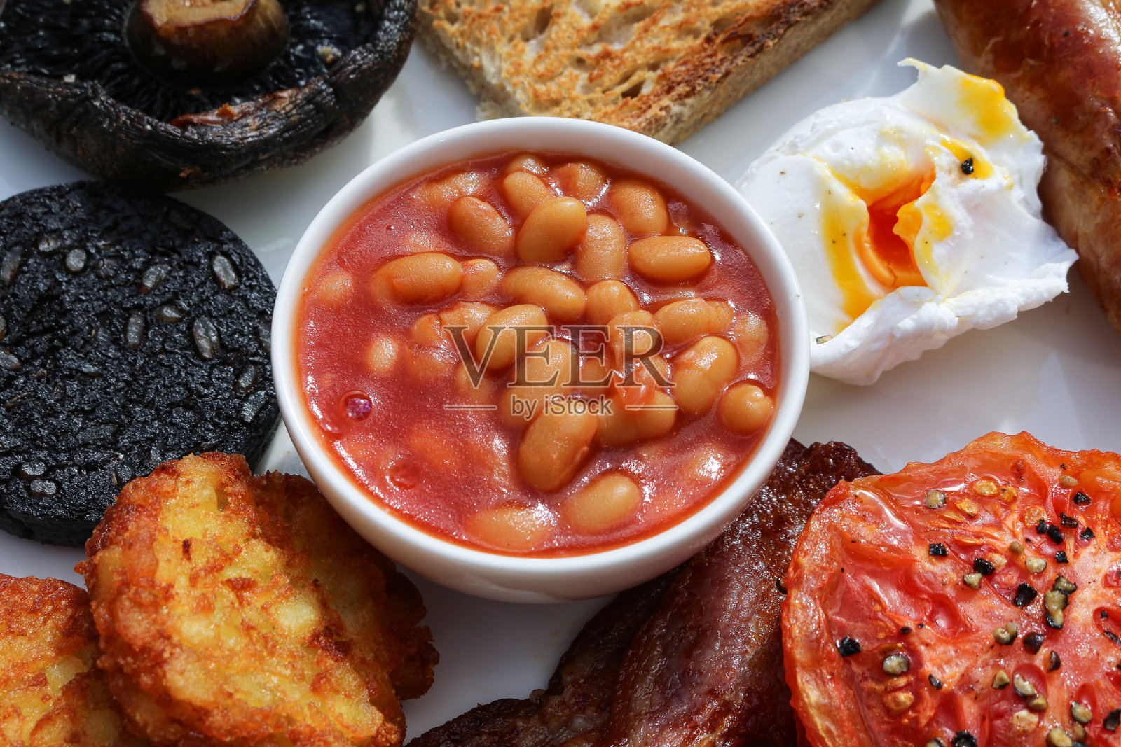 美味的英式全餐早餐，包括烤豆、番茄、荷包蛋、吐司、培根、蘑菇和土豆饼。照片摄影图片