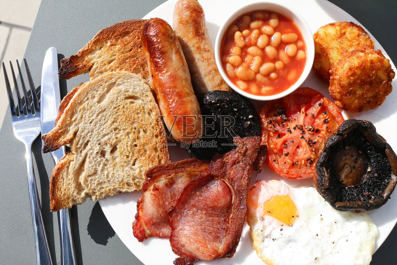 刀、叉、餐巾、煎炸早餐、吐司、香肠、培根、鸡蛋、黑布丁、蘑菇、烤豆、土豆饼的图片照片摄影图片