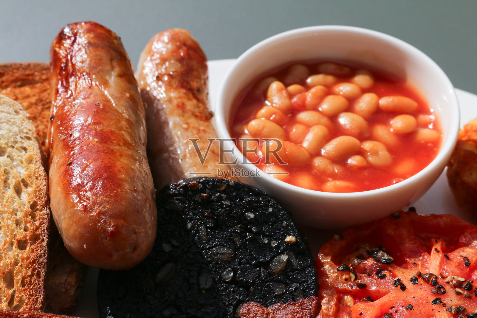 传统英式全套早餐，包含猪肉香肠、烤豆、黑布丁和番茄照片摄影图片