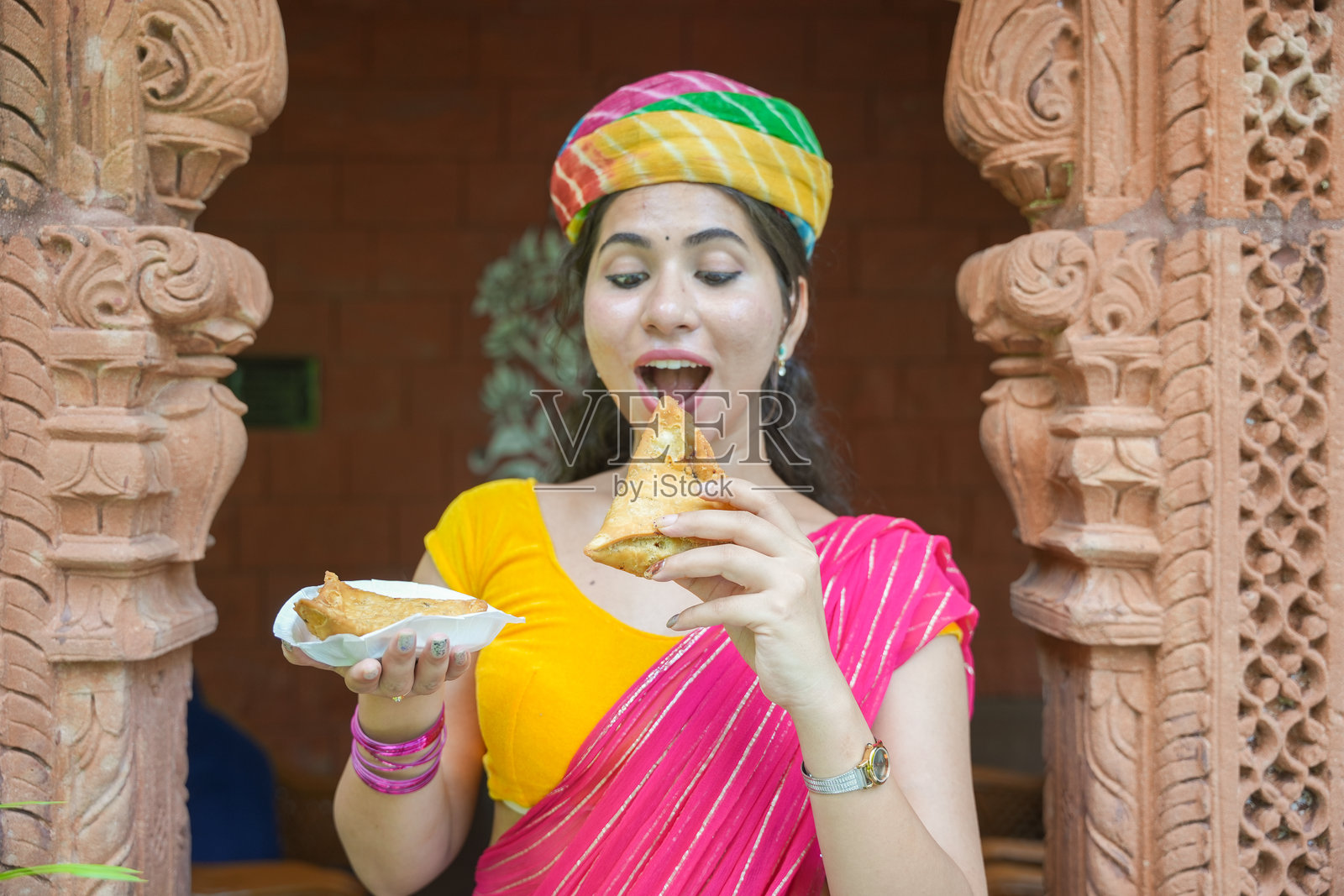 年轻快乐的印度女性穿着纱丽和头巾，正在享用印度街头美食——酥脆辛辣的萨莫萨。照片摄影图片