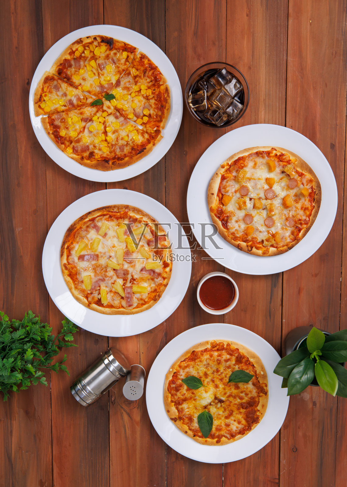 从上方俯视不同美味可口的脆皮披萨组合，白色盘子上的平面面包装饰，木桌上，黑色背景下摆放着自制烹饪材料，食品广告。照片摄影图片