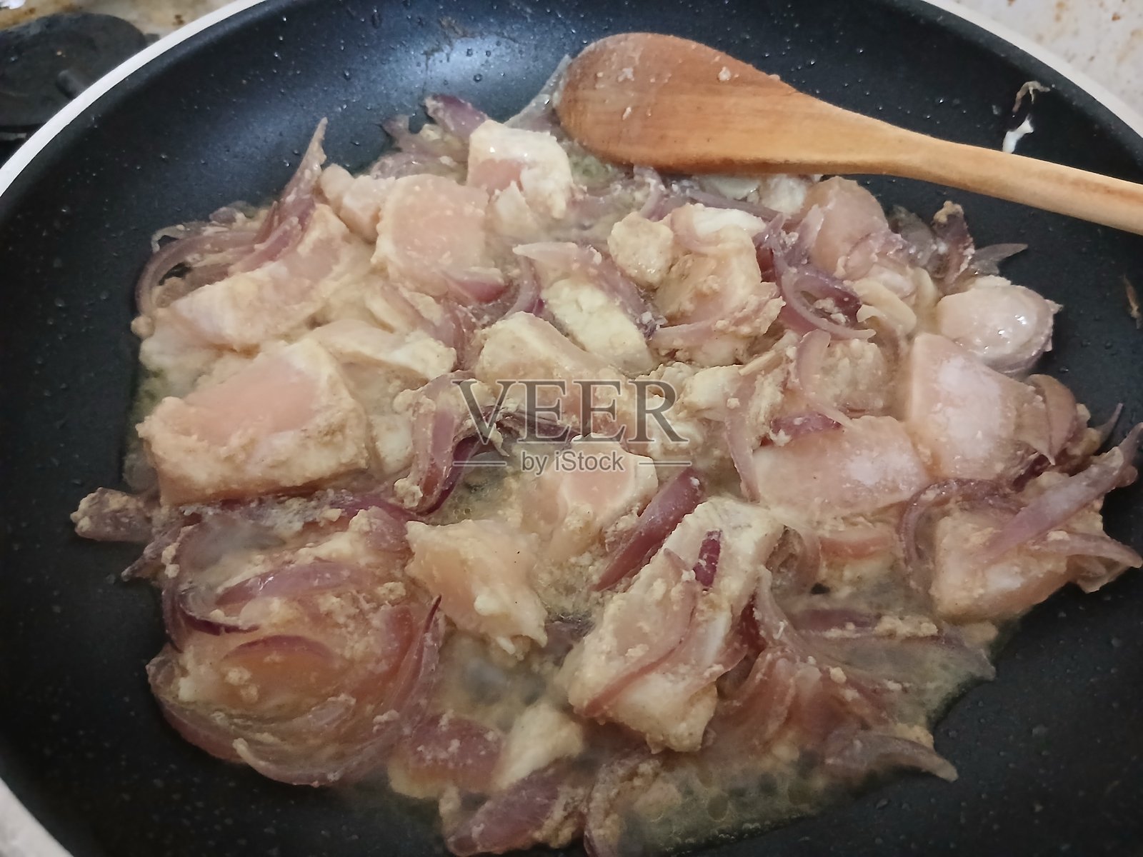 用木勺在黑色平底锅中用植物油炒洋葱的鸡胸肉片照片摄影图片