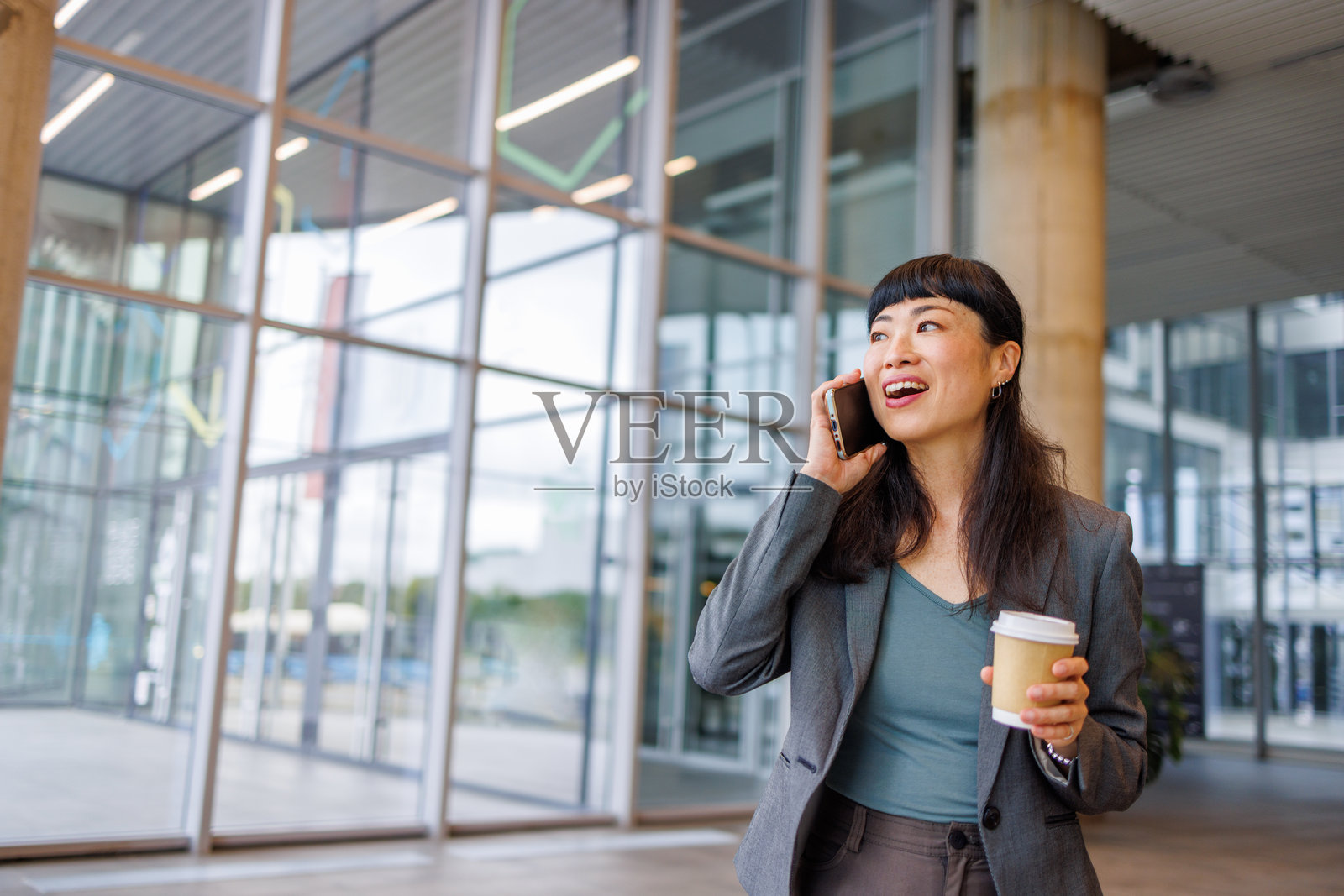 快乐的女商人在现代办公室里一边打电话一边喝咖啡照片摄影图片