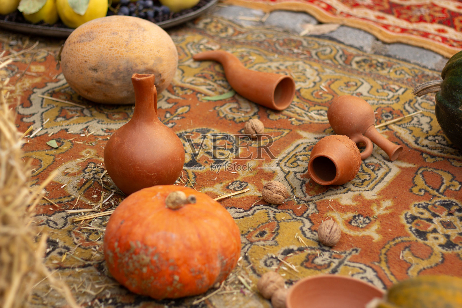 橙色南瓜、哈密瓜、陶土壶、陶瓷酒壶放在民族地毯上照片摄影图片
