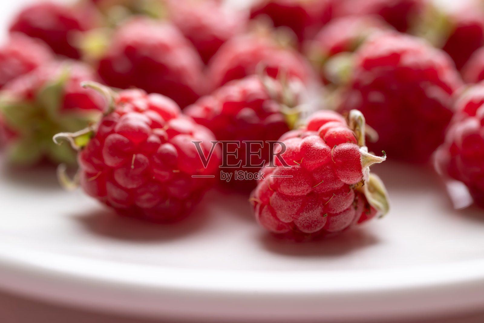 新鲜的覆盆子和叶子放在白色盘子上，夏季水果照片摄影图片