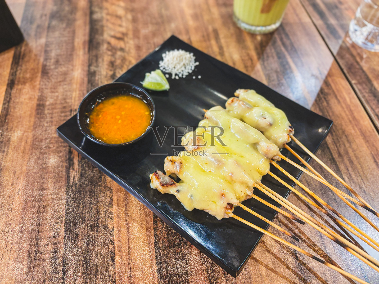 烤鸡肉沙爹串上丰盛的融化奶酪，搭配鲜艳的蘸酱和撒上美味的芝麻，盛放在光滑的黑色盘子上，令人愉悦的融合美食。照片摄影图片