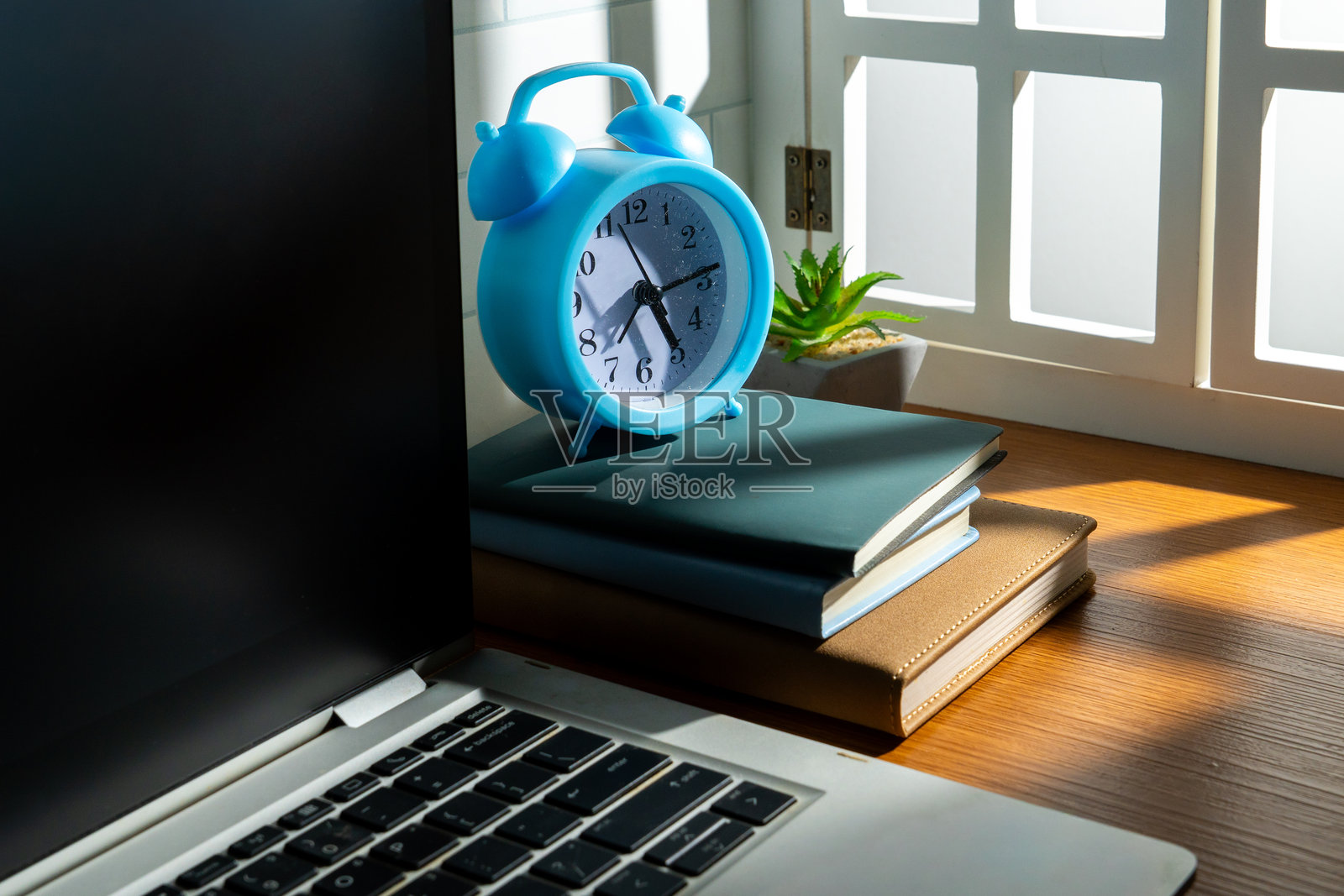 一张木质书桌，上面有一台笔记本电脑、几本书、一个闹钟和一盆多肉植物。照片摄影图片