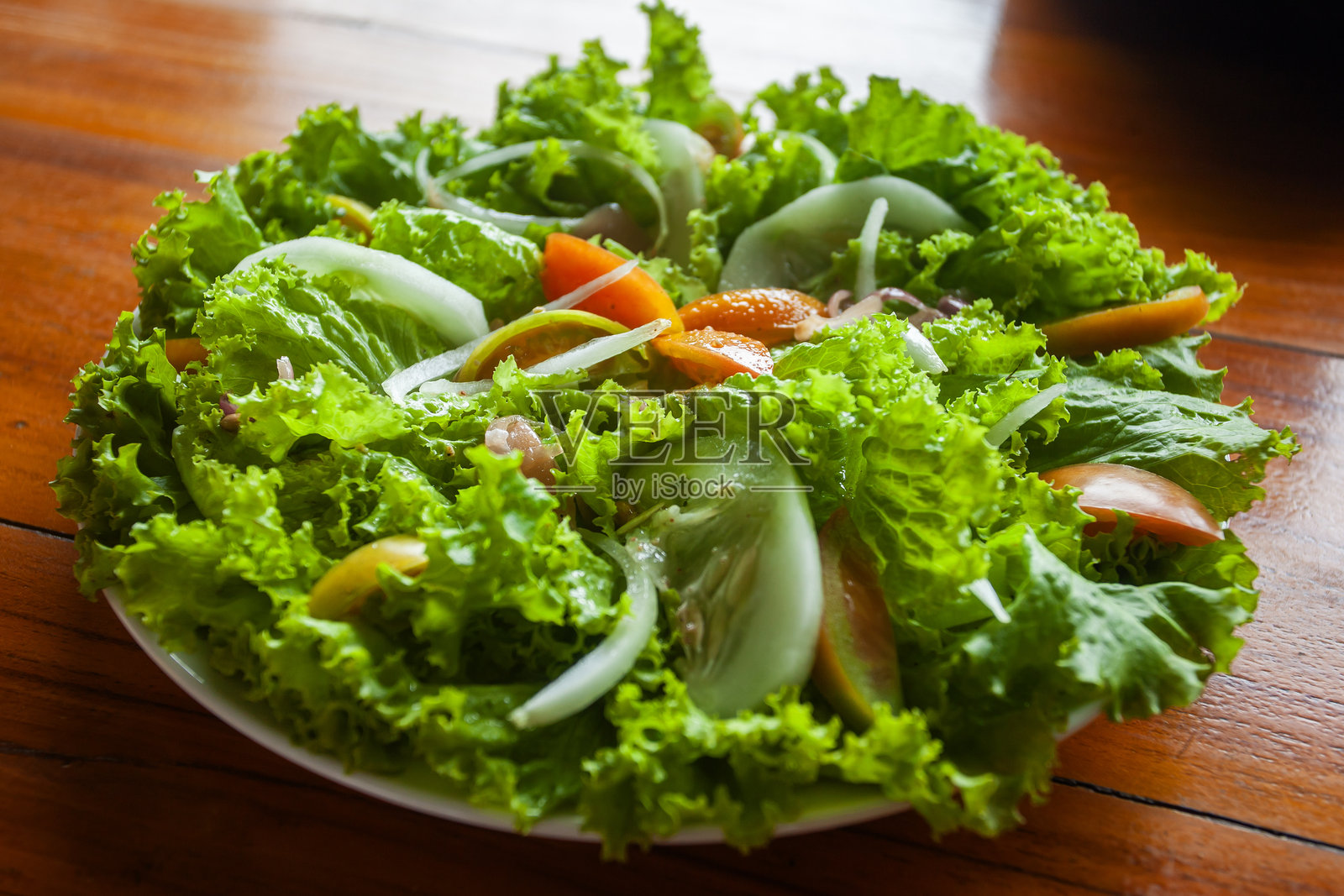东帝汶的新鲜蔬菜沙拉，作为健康的配菜。由脆嫩的生菜、切片番茄、黄瓜和洋葱组成，摆放在木桌背景的盘子上。照片摄影图片