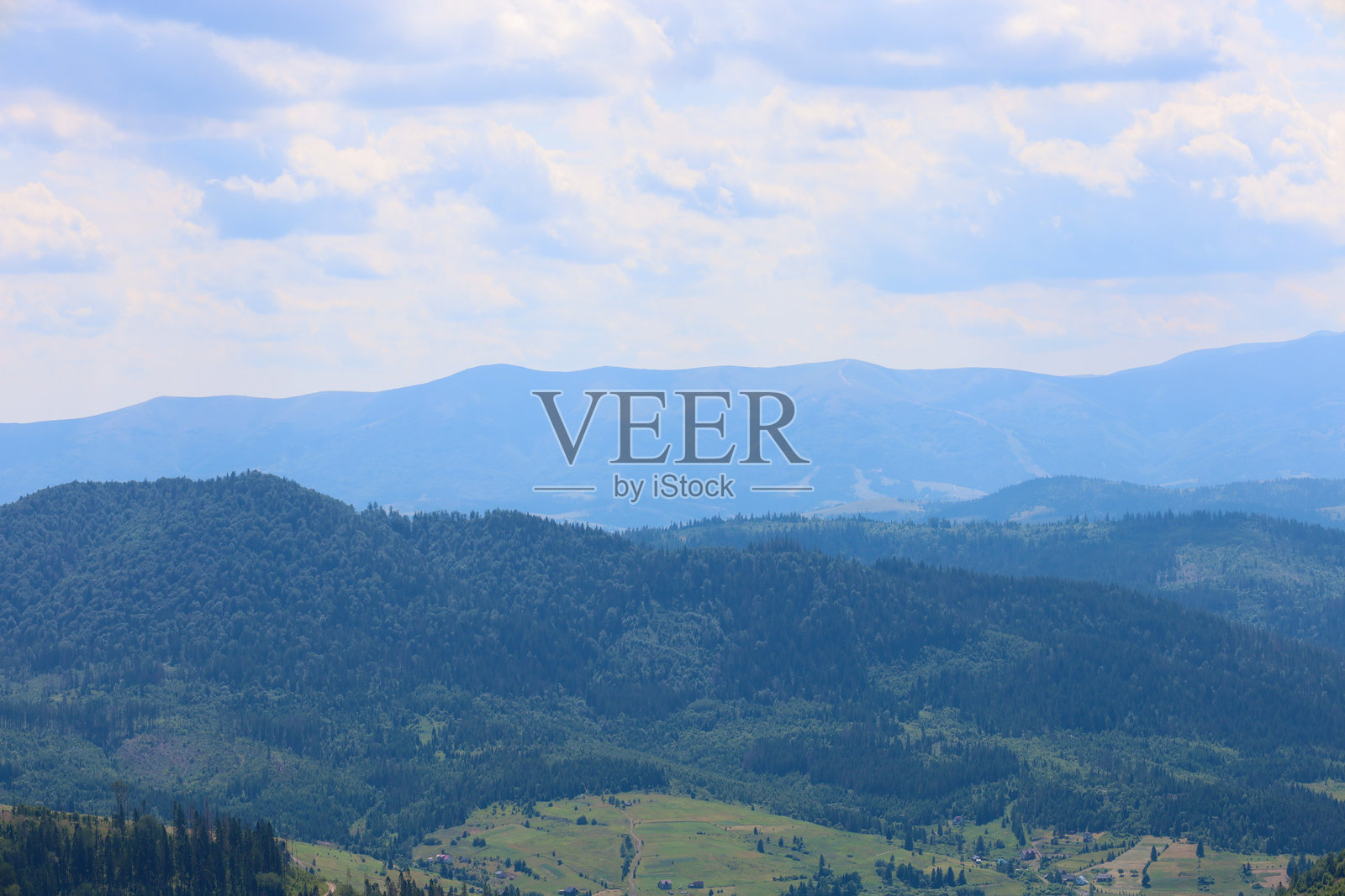 一幅分层的山脉风景，森林覆盖的山坡向远处的蓝色山峰延伸。这幅图像传达了自然的宁静与壮丽，展现了在广阔的蓝天和蓬松的白云下，自然的无边无际与美丽。照片摄影图片