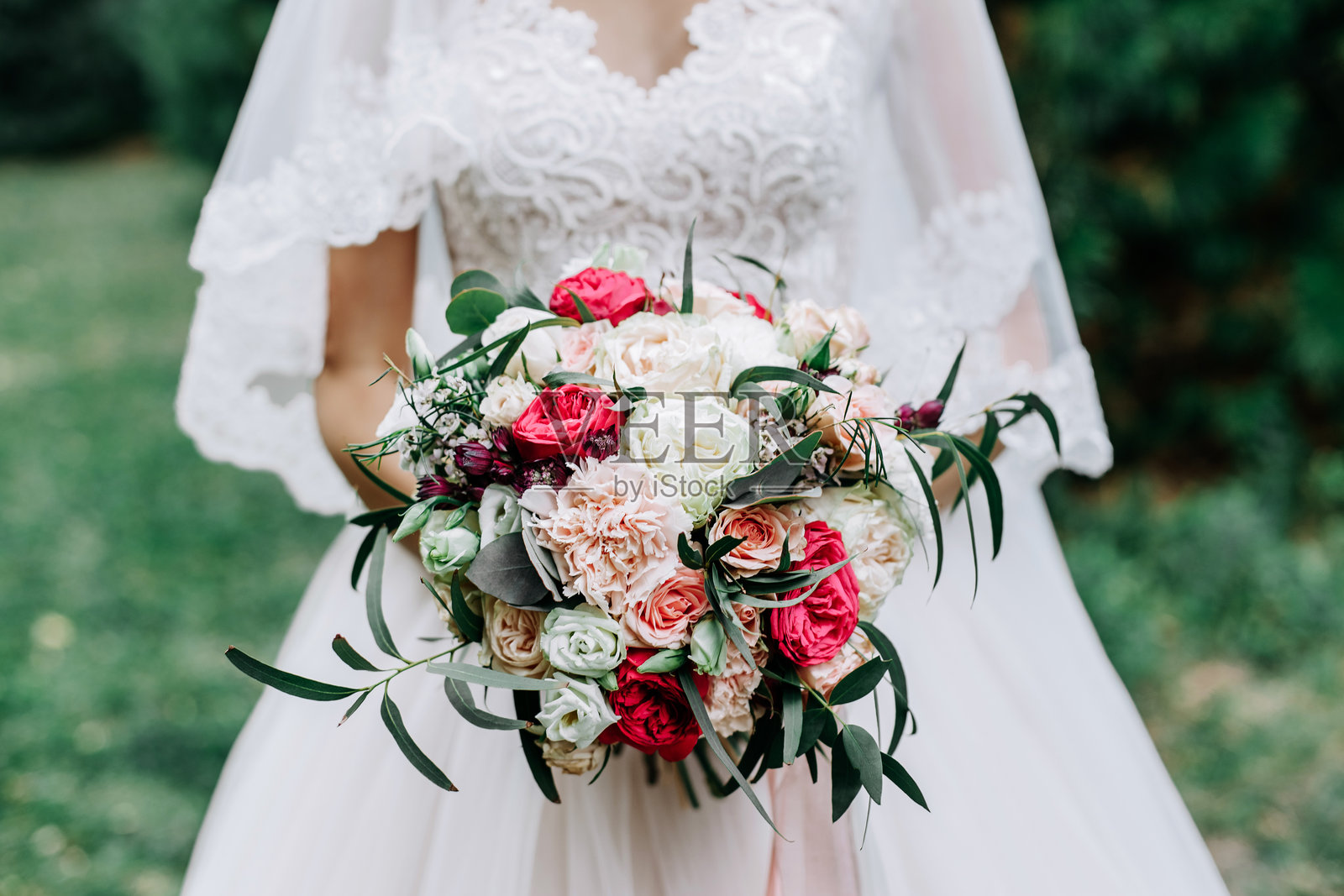 美丽的新娘手捧着一束由红色、白色和米色玫瑰组成的华丽婚礼花束照片摄影图片