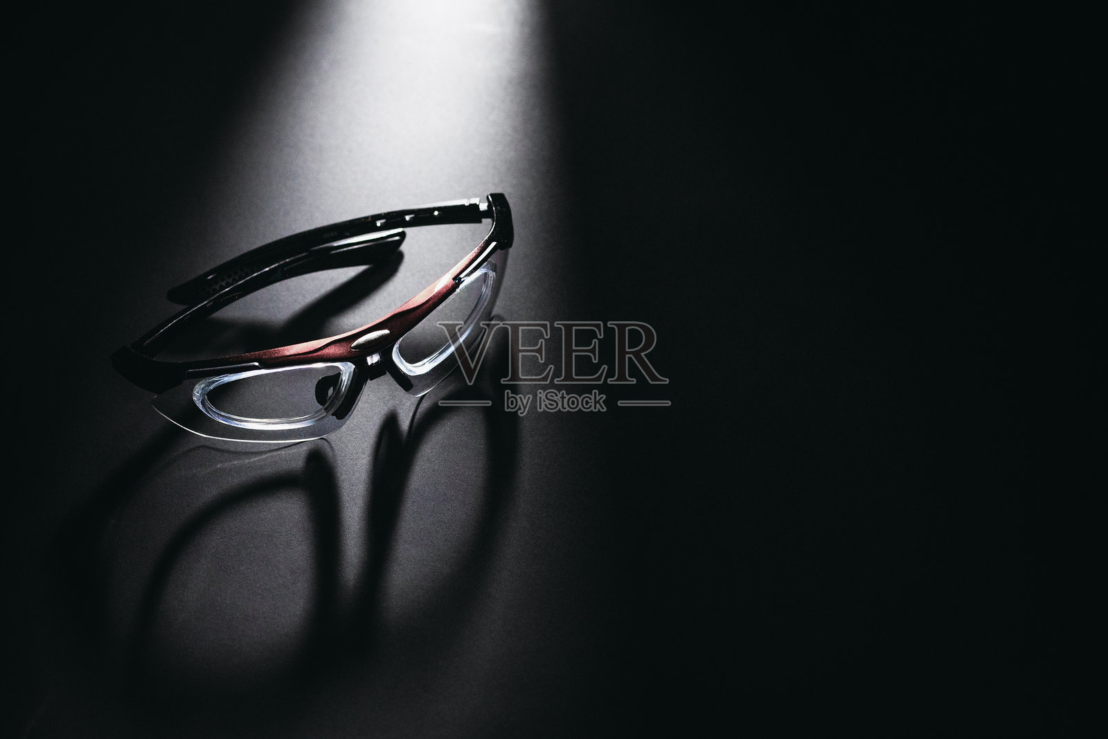 时尚现代的眼镜放置在黑色反光表面上，灯光照射下。照片摄影图片