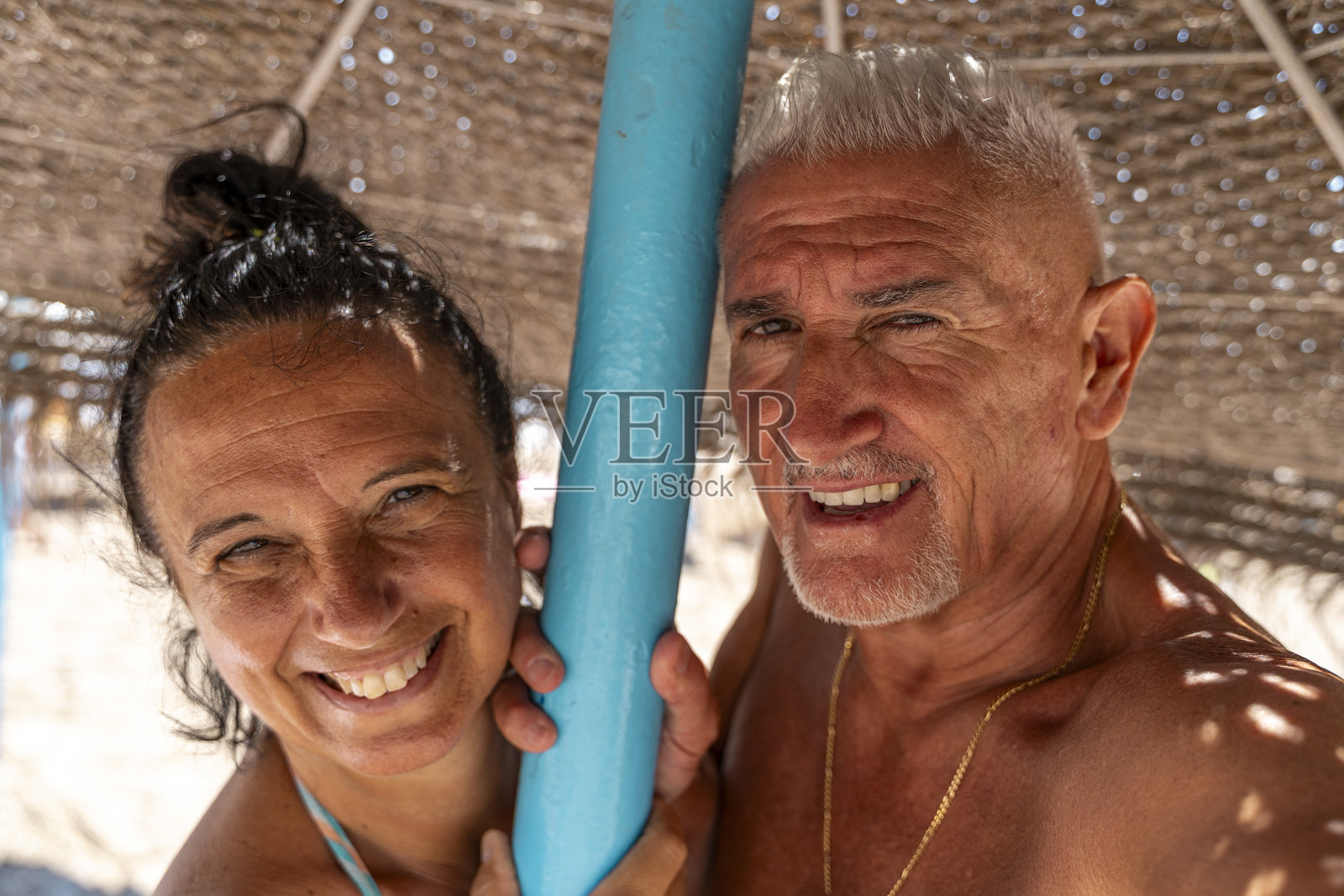 一对快乐美丽的退休夫妇在海滩的草伞下拥抱微笑，拍摄自拍照，享受夏季假期。照片摄影图片