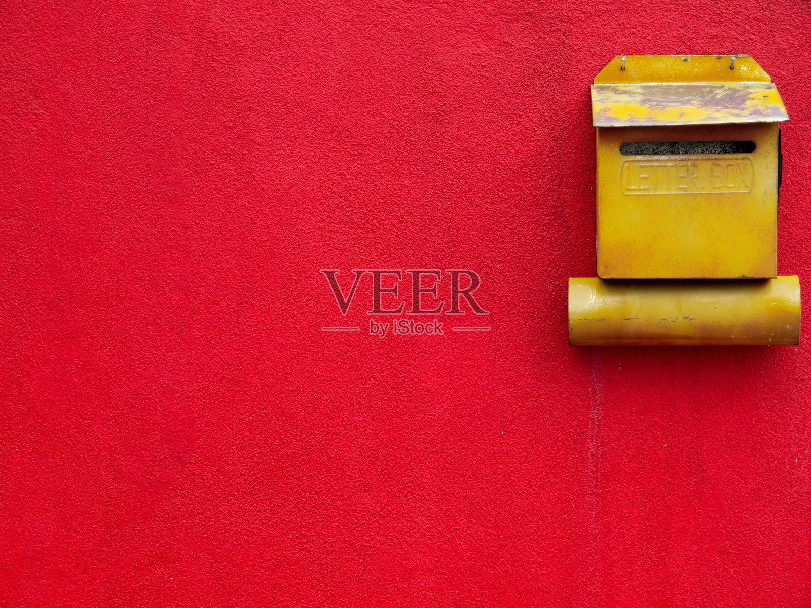 红色粗糙纹理的墙壁上有一个黄色金属信箱。照片摄影图片