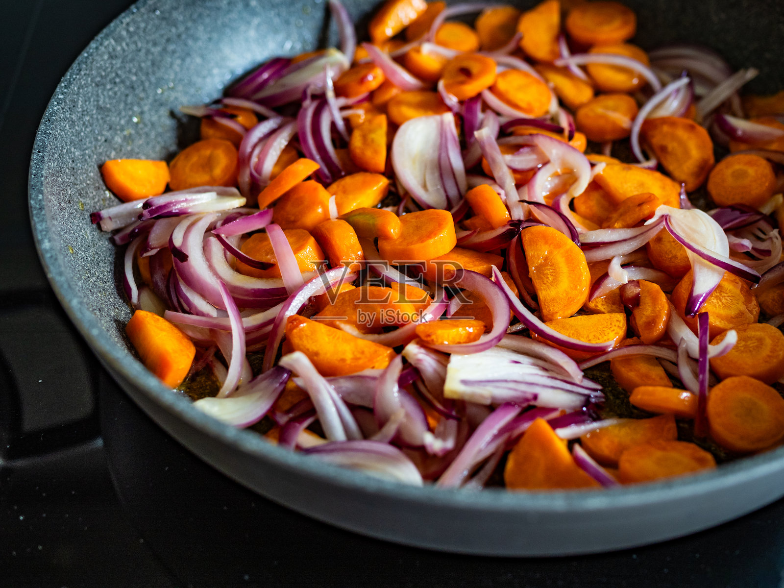 在电磁炉上用煎锅炒胡萝卜和红洋葱照片摄影图片