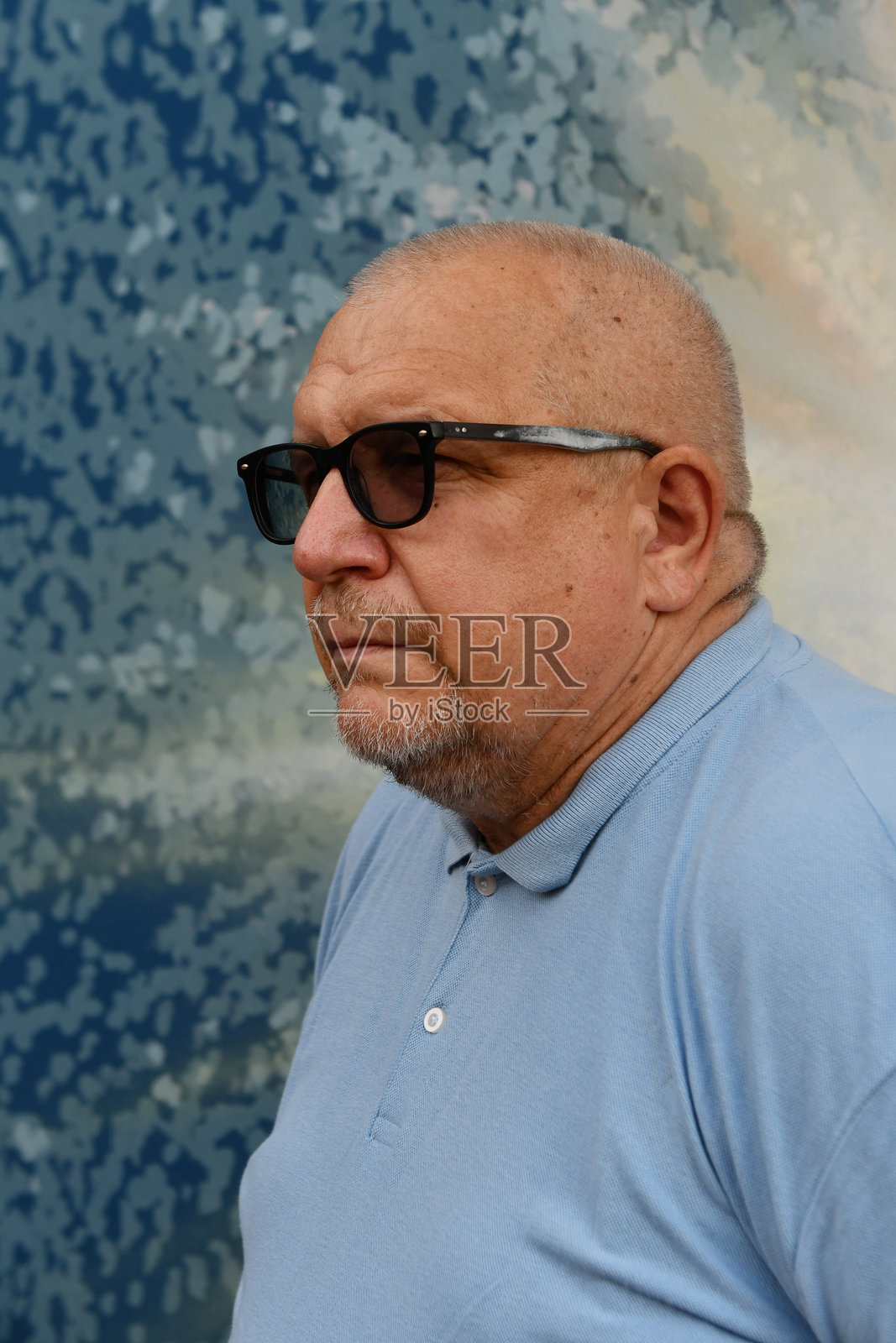 一位年长的灰发白人男性，留着胡须，戴着太阳镜，穿着蓝色T恤。照片摄影图片