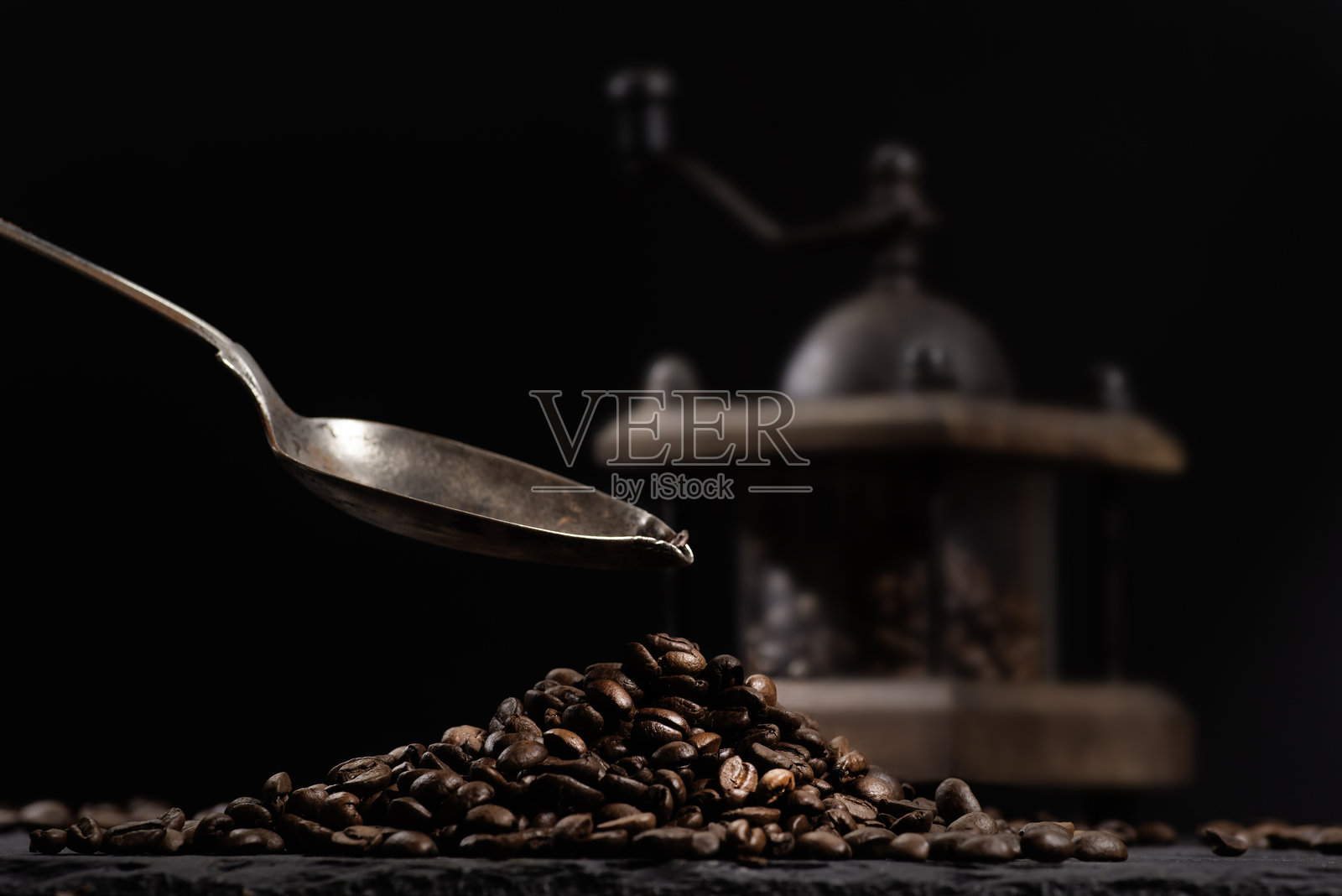 新鲜咖啡豆在咖啡研磨机中的特写，旁边是放在石质桌面上的咖啡豆。一只勺子正在倒咖啡。照片摄影图片