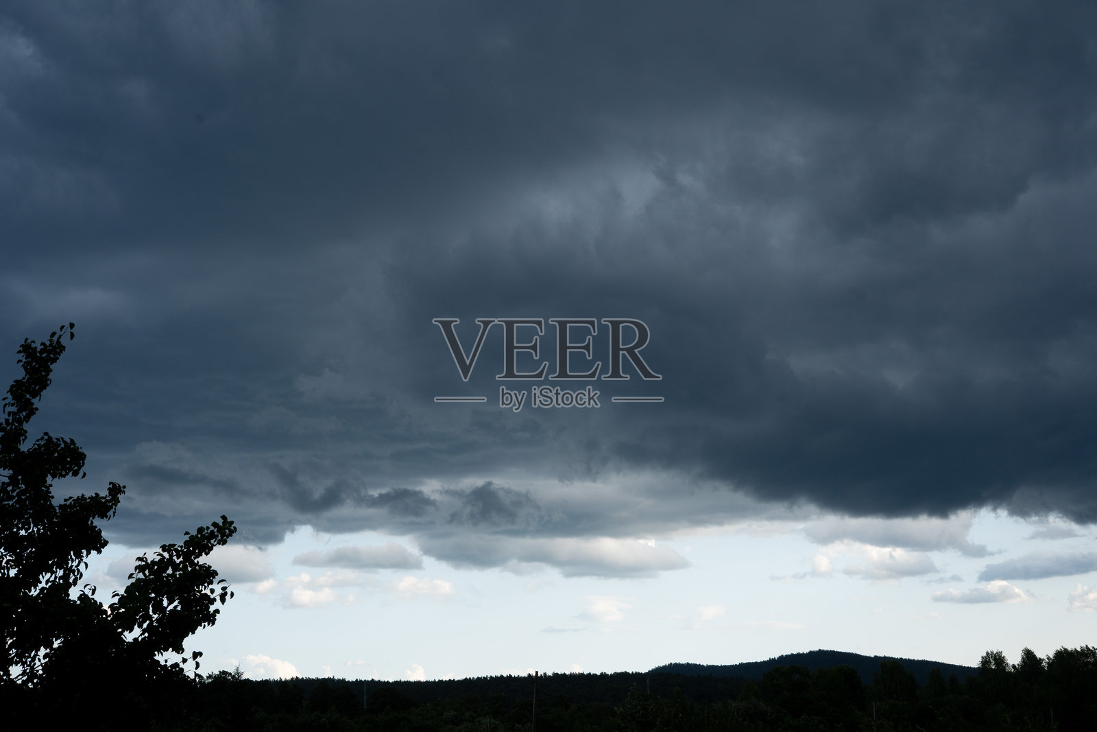 黄昏时分，动荡的黑云在远处的山脉上空盘旋，形成戏剧性的天空景观。照片摄影图片