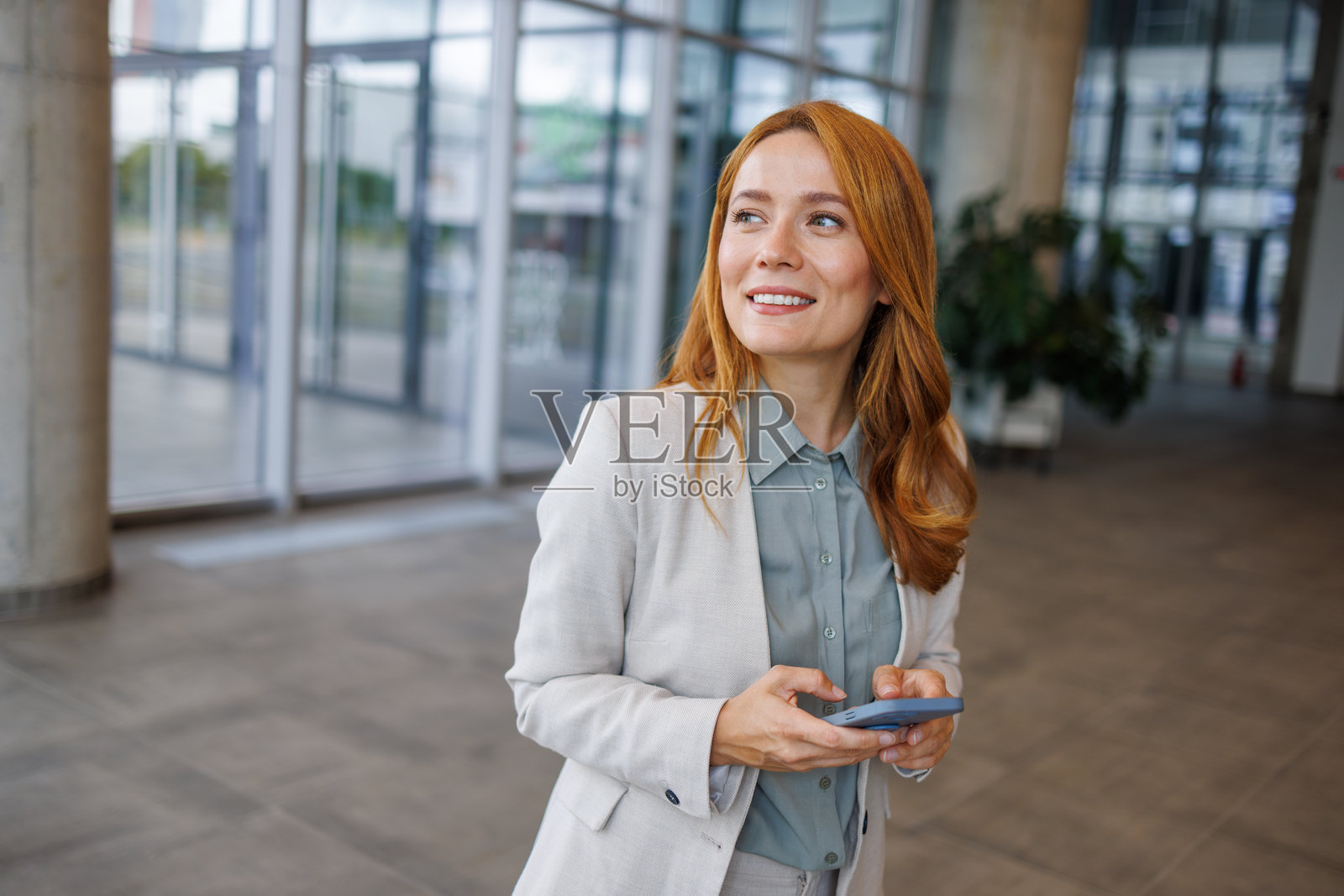 微笑的女商人在现代办公大楼中使用智能手机照片摄影图片