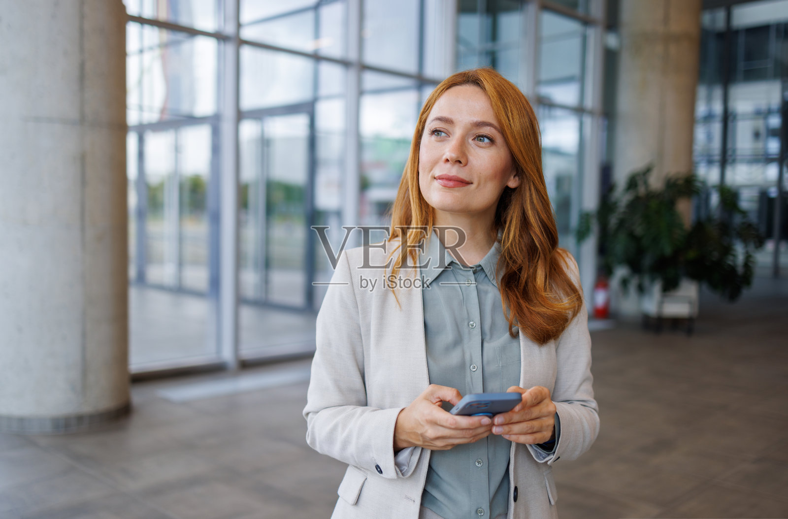 商务女性在现代办公大楼中使用智能手机并向一旁看去照片摄影图片