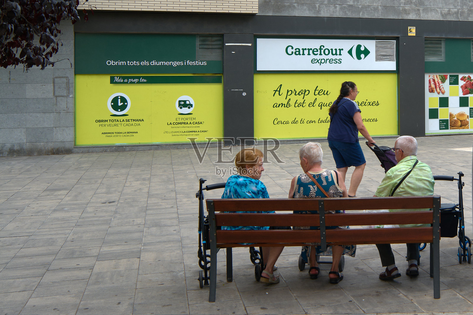 人们坐在家乐福商店外的长椅上。照片摄影图片