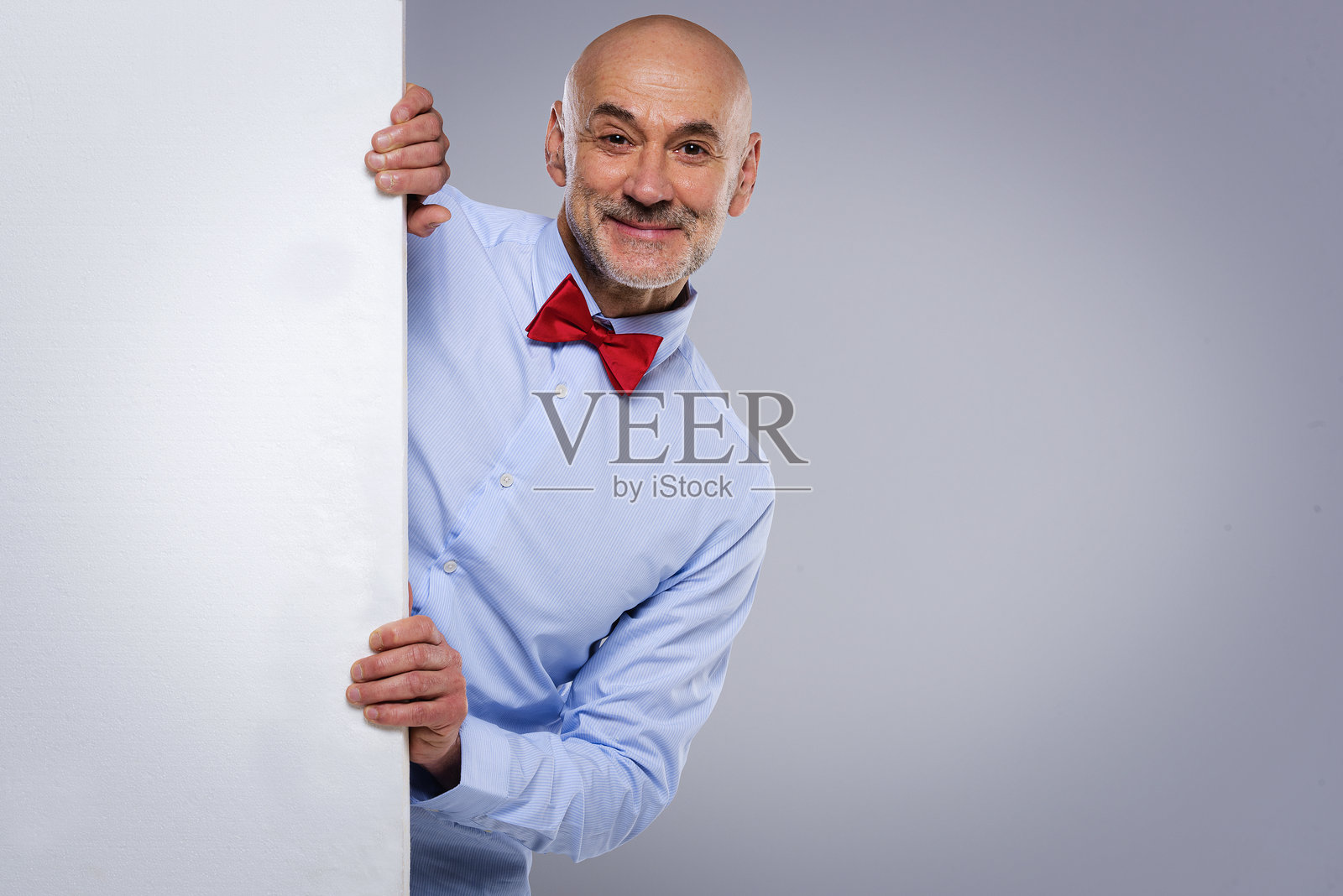 一个中年男子站在白色墙后面，探出头来。照片摄影图片