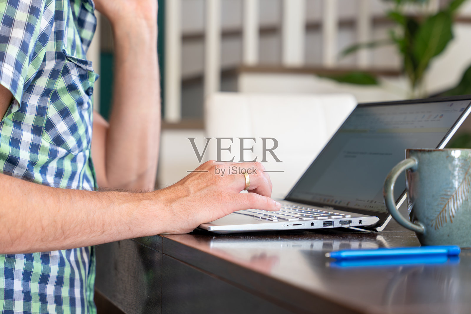 在室内使用笔记本电脑工作，桌上放着咖啡杯，代表远程工作和数字生产力照片摄影图片