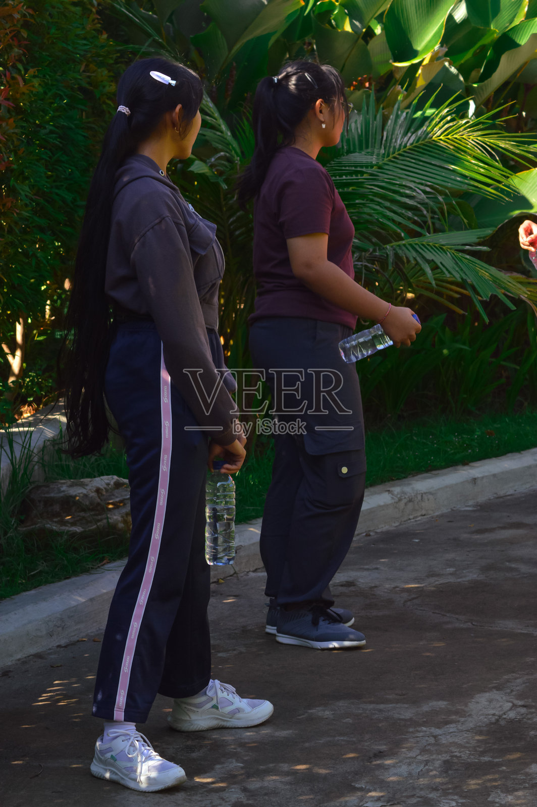 两个女孩手持水瓶站在花园小径上照片摄影图片