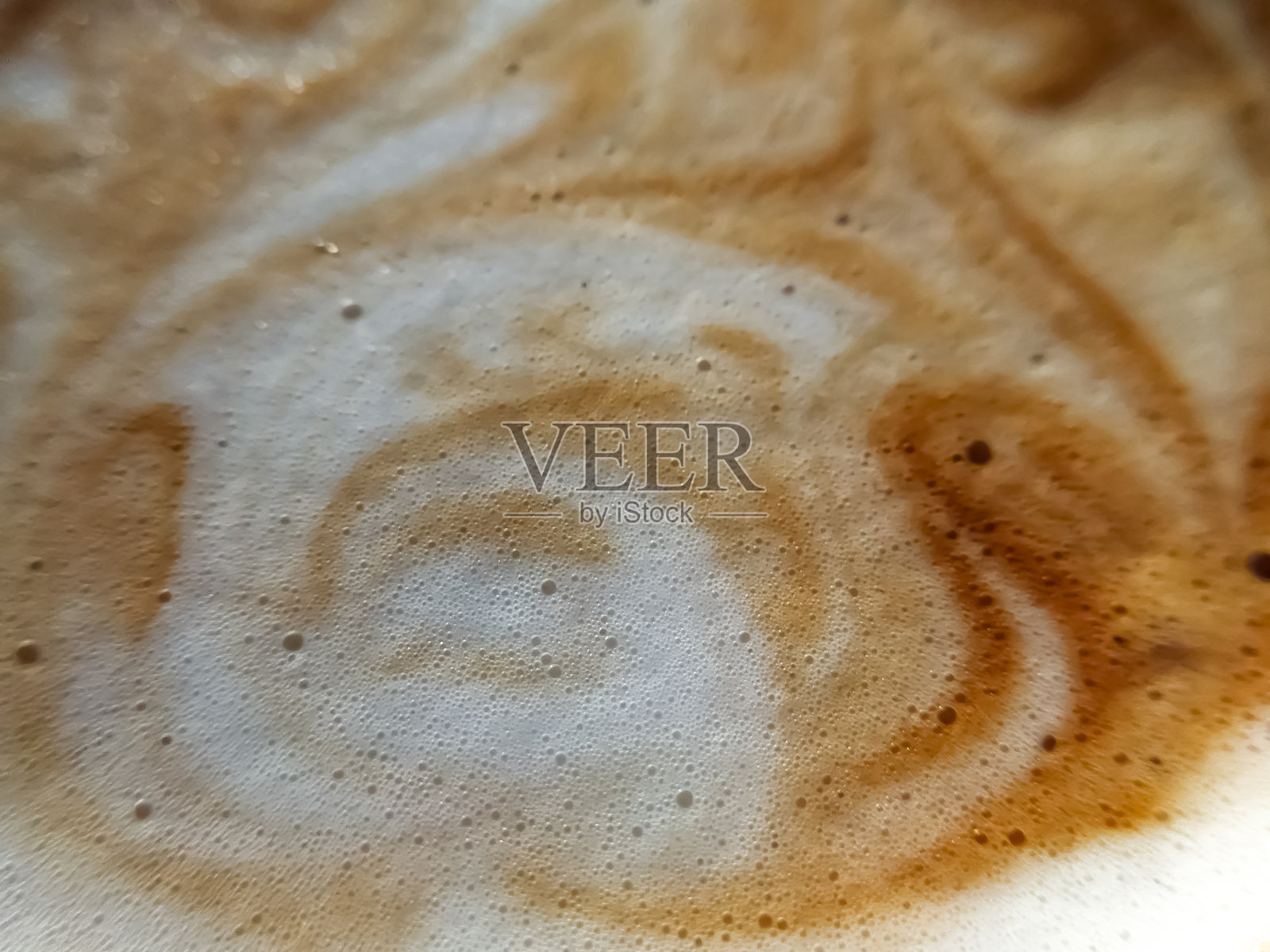 高角度全景拍摄的咖啡与牛奶交融，展现出泡沫气泡，形成迷人的抽象图案。照片摄影图片