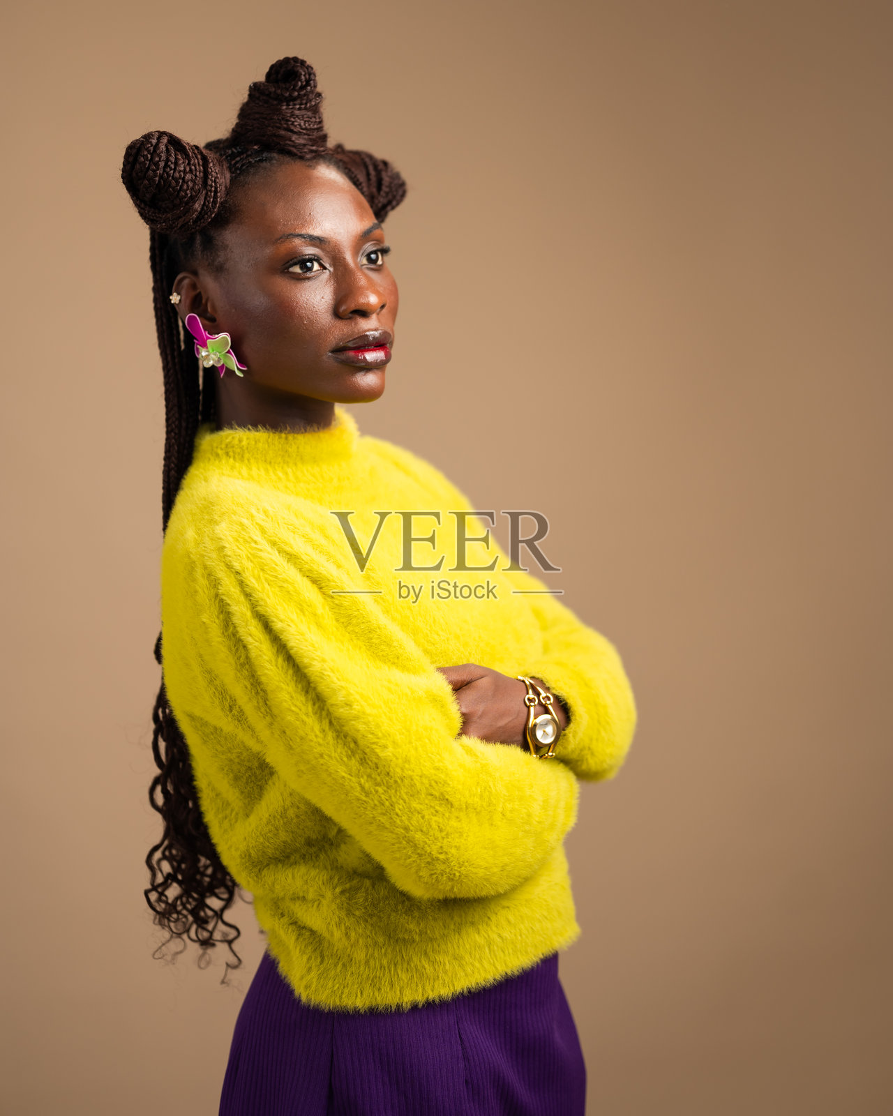 自信的非洲女性穿着明亮的黄色毛衣和紫色裙子，双臂交叉，深思熟虑地凝视前方，她的大胆发型和醒目的耳环增添了现代优雅感。照片摄影图片