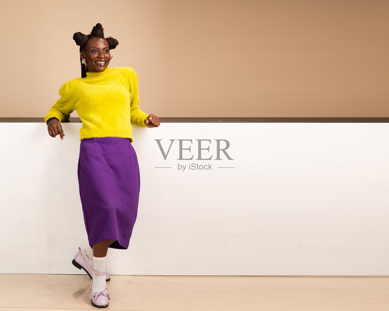 微笑的非洲女性在工作室的白色墙壁上悠闲地倚靠着照片摄影图片